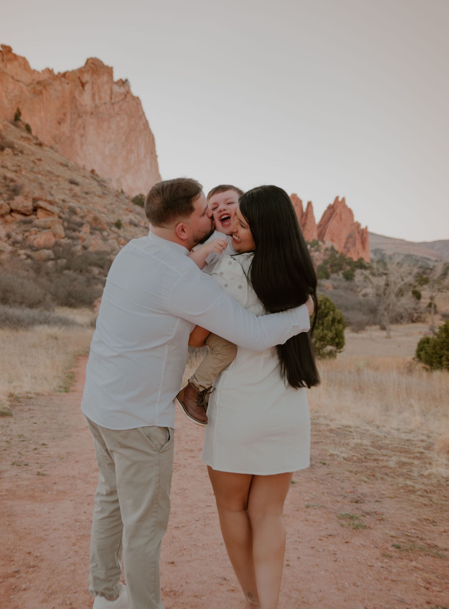 A happy family of three shares a joyful moment on a desert trail with stunning rock formations at Garden of the Gods.