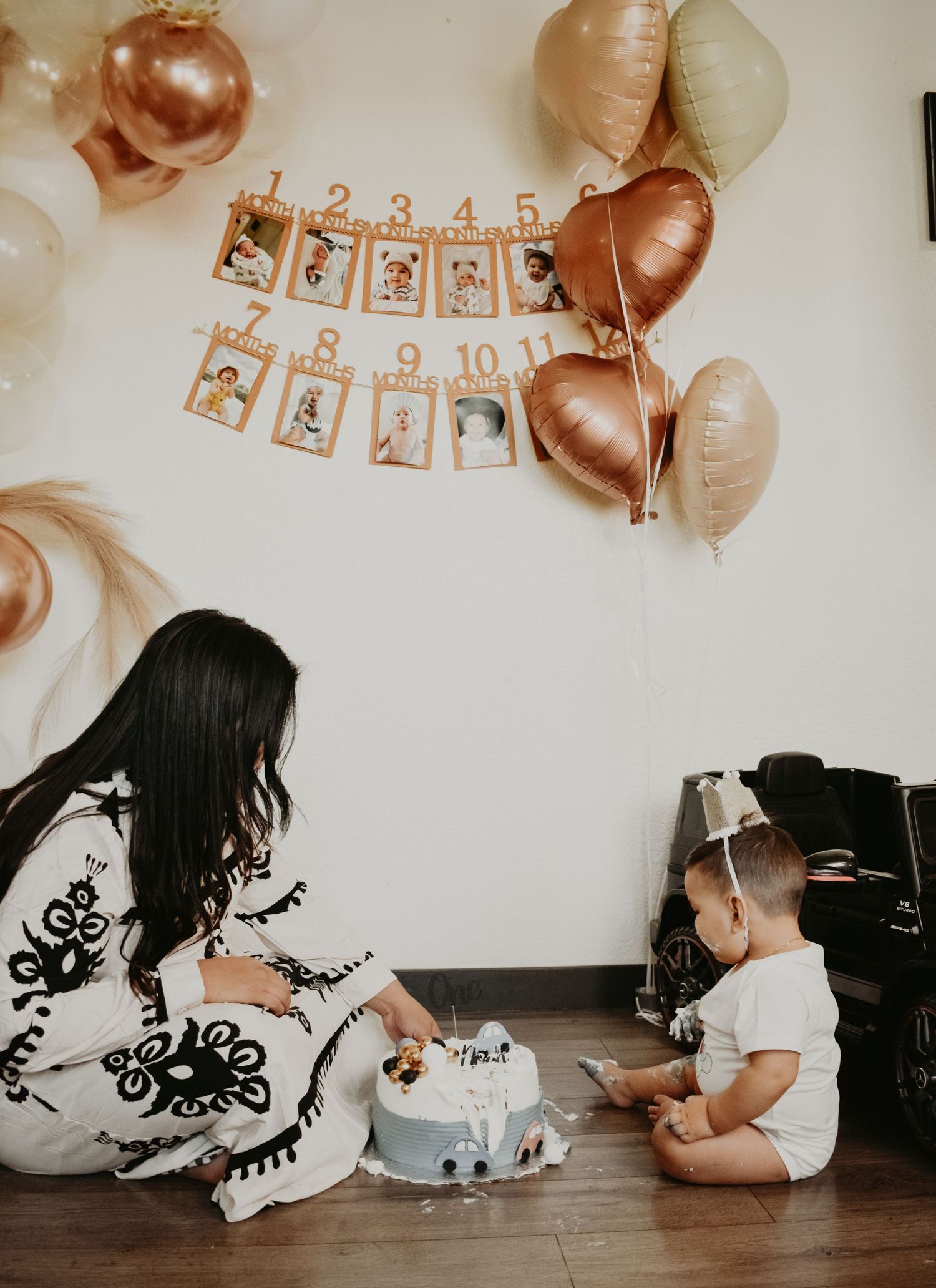 Mother and baby celebrating first birthday with monthly photo banner and rose gold balloons.