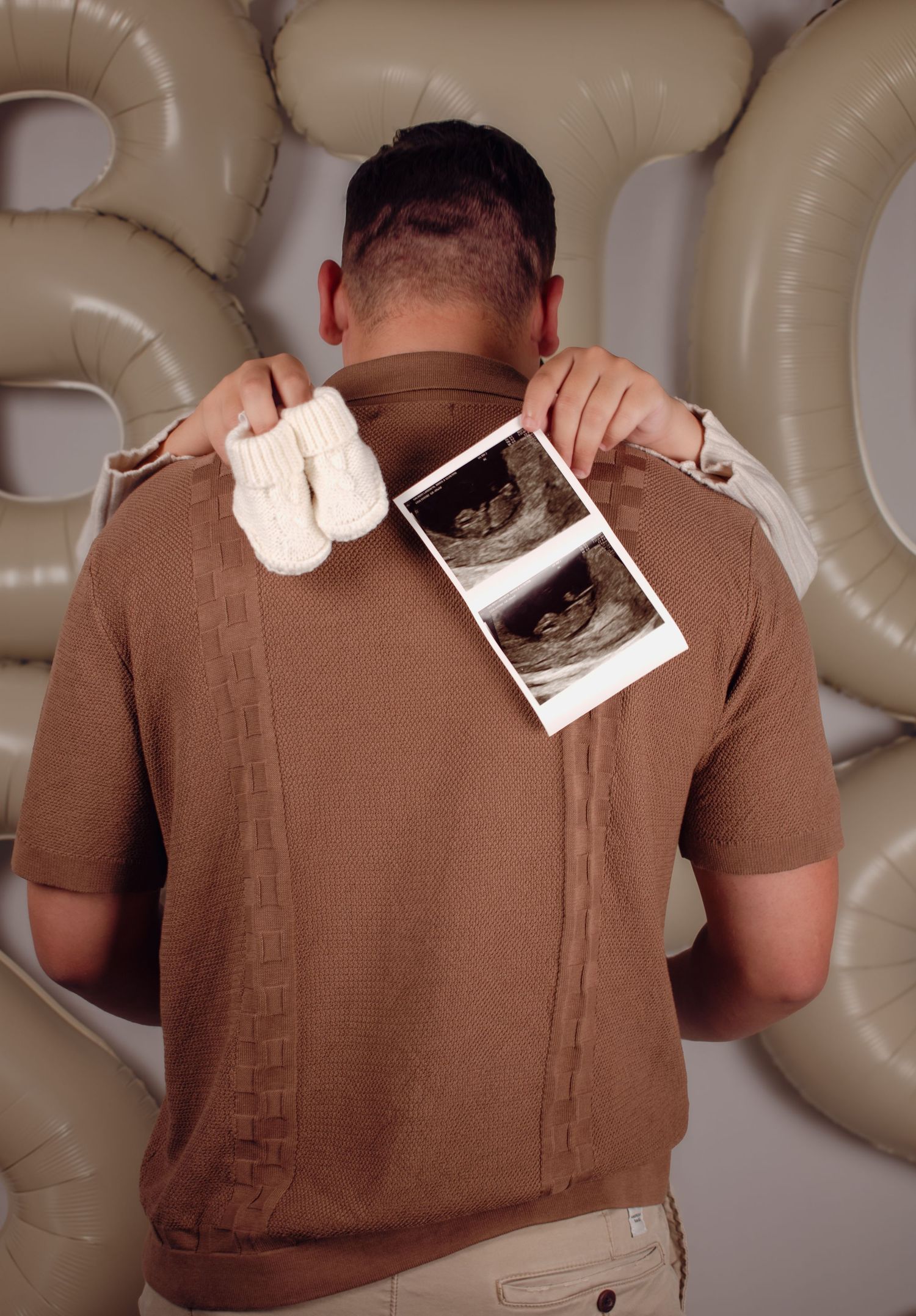 Man holding baby ultrasound photo and tiny booties behind his back for a pregnancy announcement.