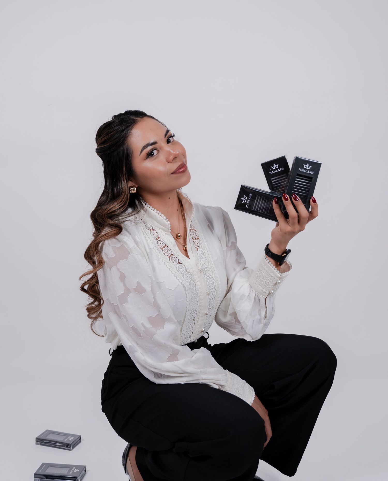 Woman in white blouse and black pants holding dark product boxes, posing against a light gray background.