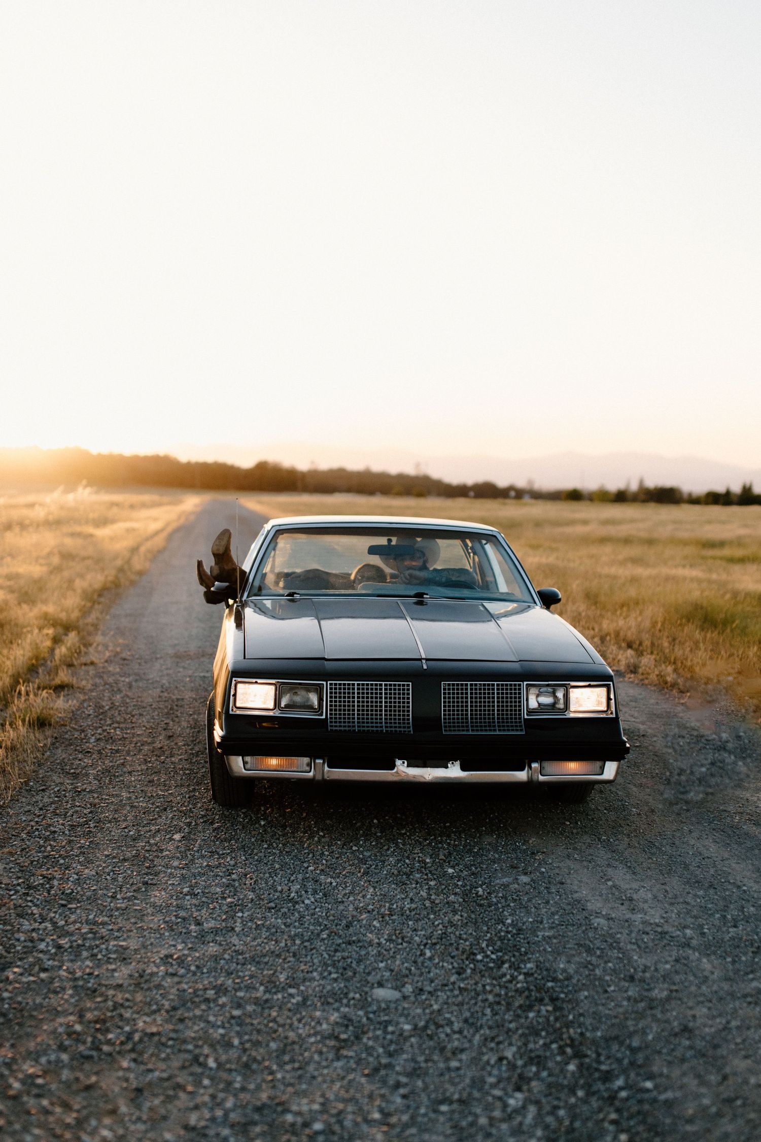 Couple posing with a classic car during their engagement session in a field in Northern California, captured by Makayla Miranda Photo.