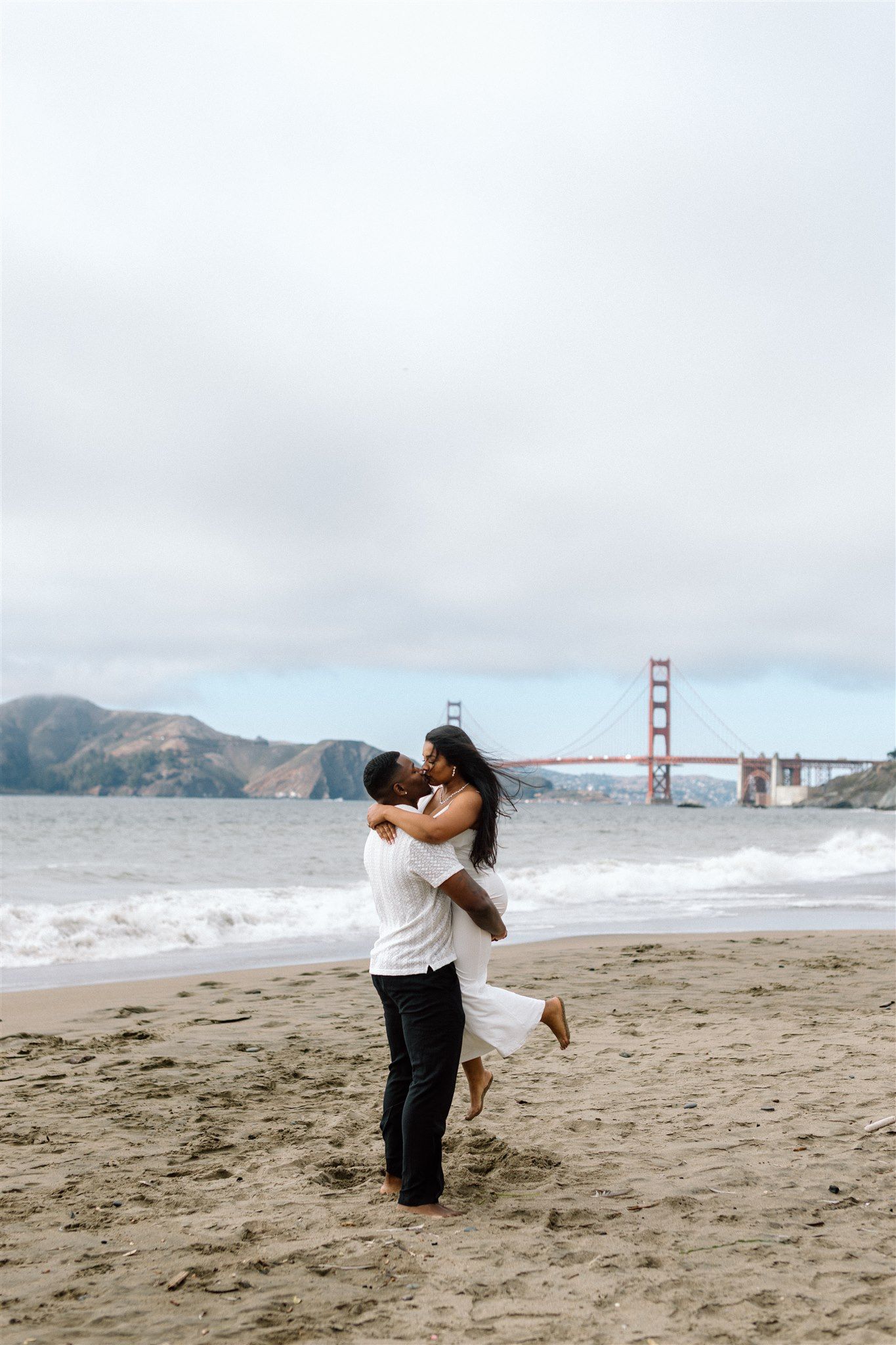 Couple posing for their engagement session at Baker Beach in San Francisco, California, captured by Makayla Miranda Photo