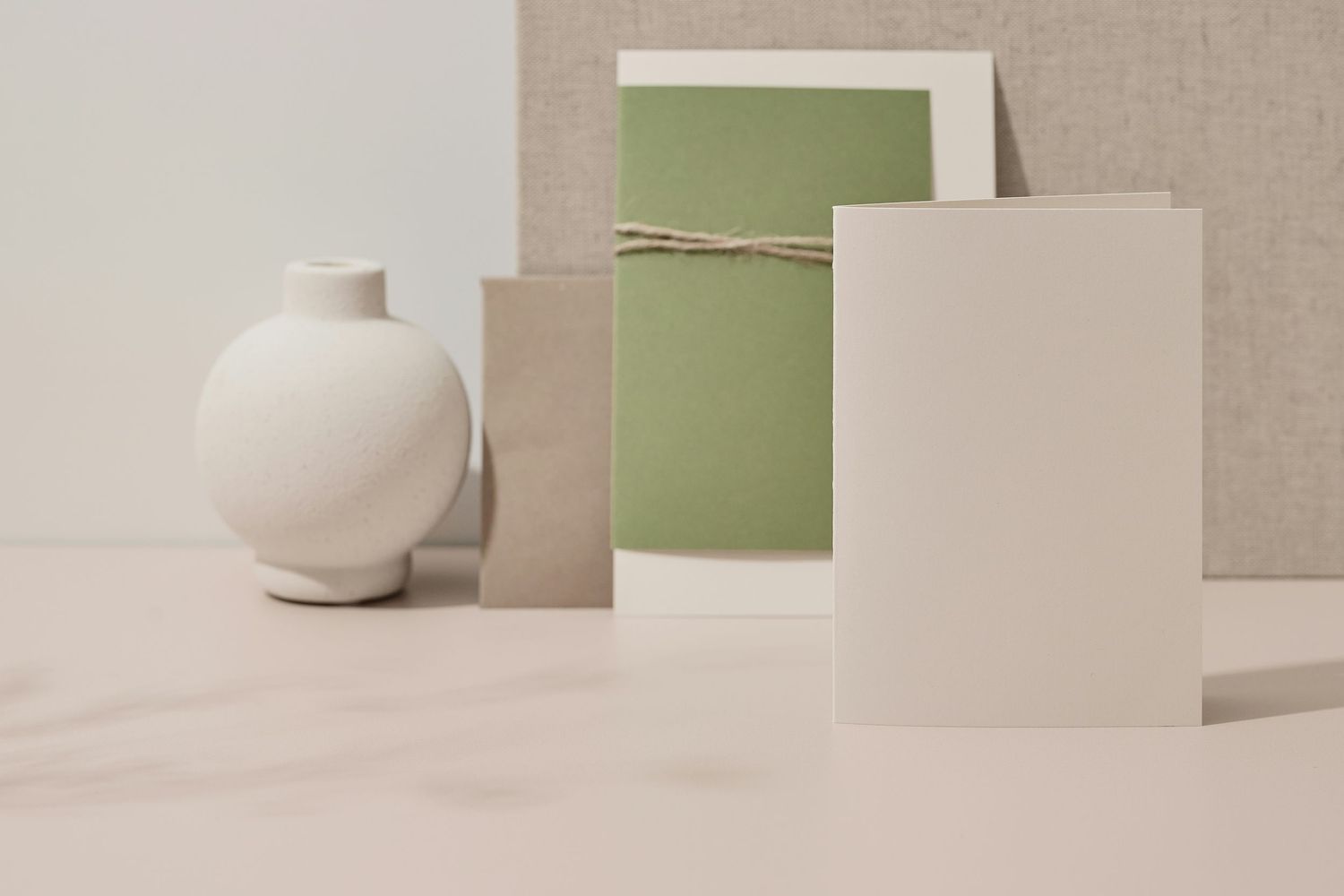 Minimalist stationery flat lay with white ceramic vase, sage green and beige cards on marble surface.