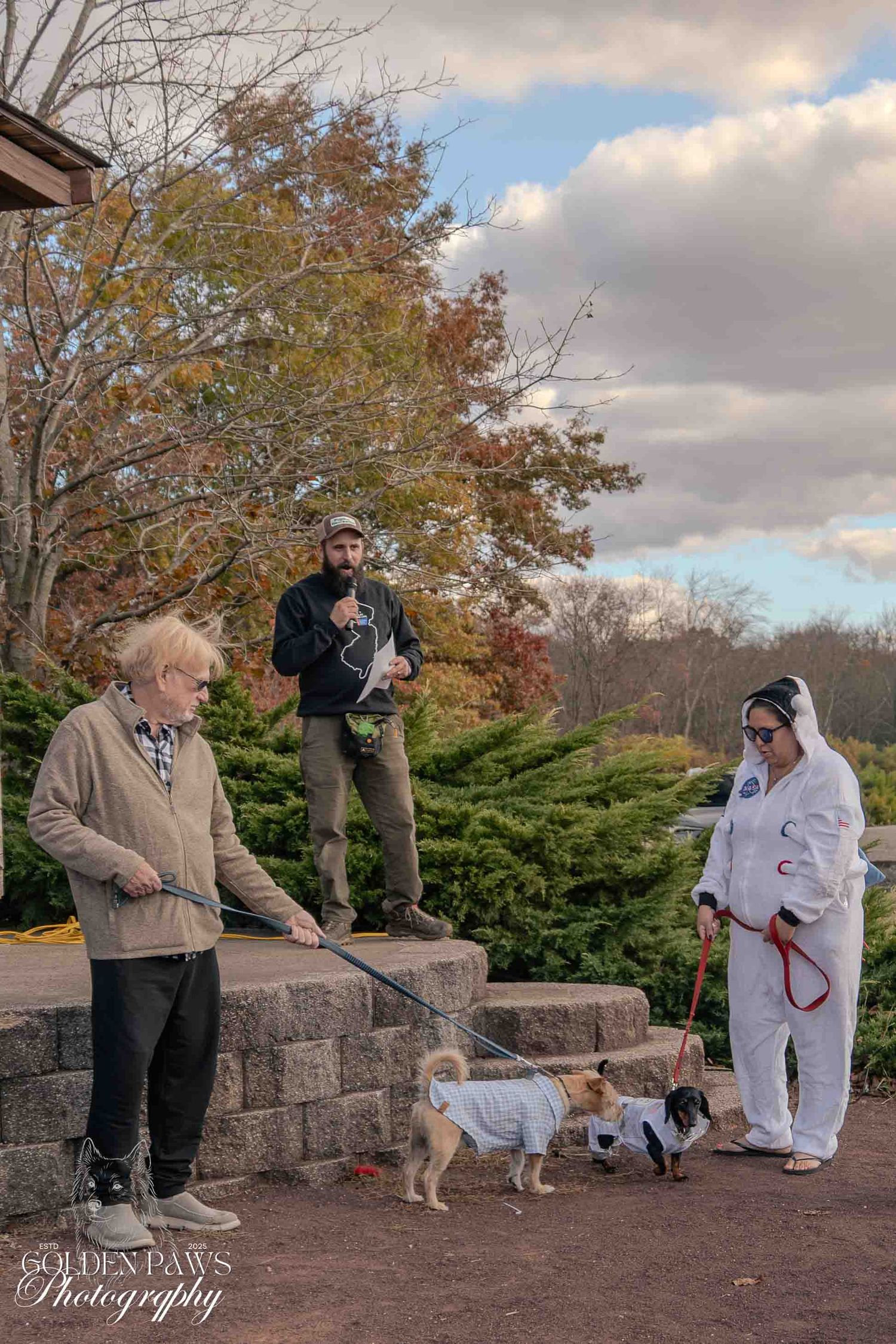 Three people with small dogs in Halloween costumes outdoors at a park during autumn, photographed by Golden Paws Photography.
