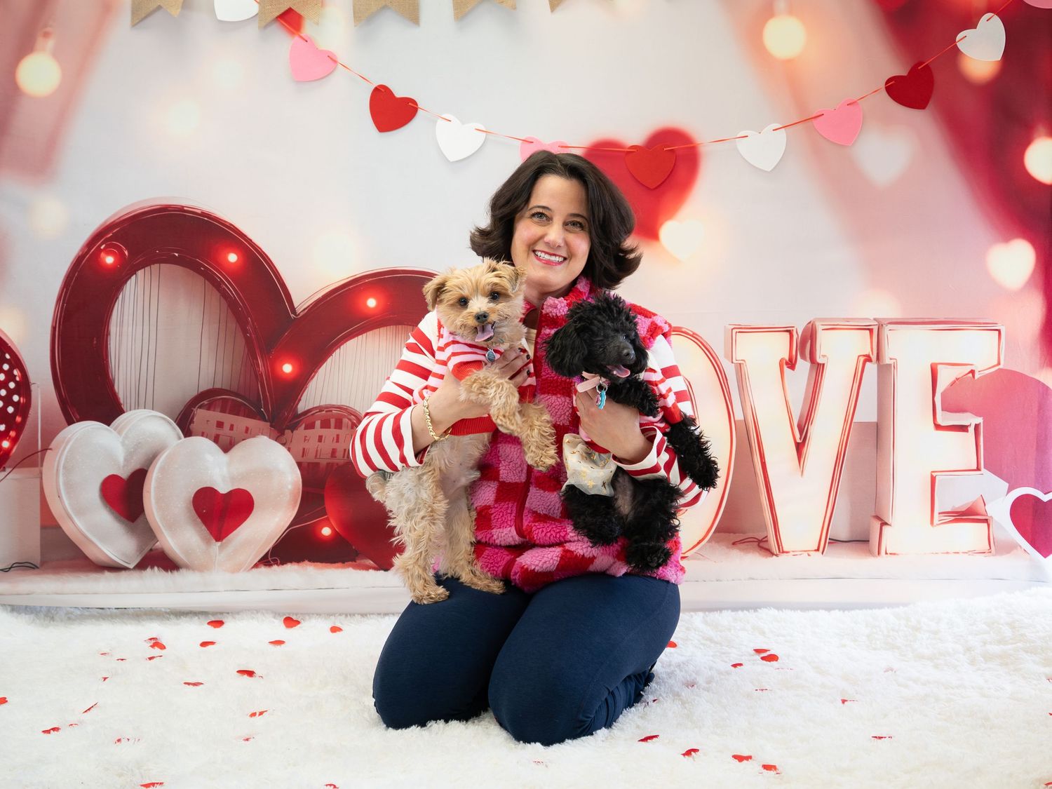 Woman holding two dogs in Valentine's Day themed photo with LOVE letters and heart decorations.