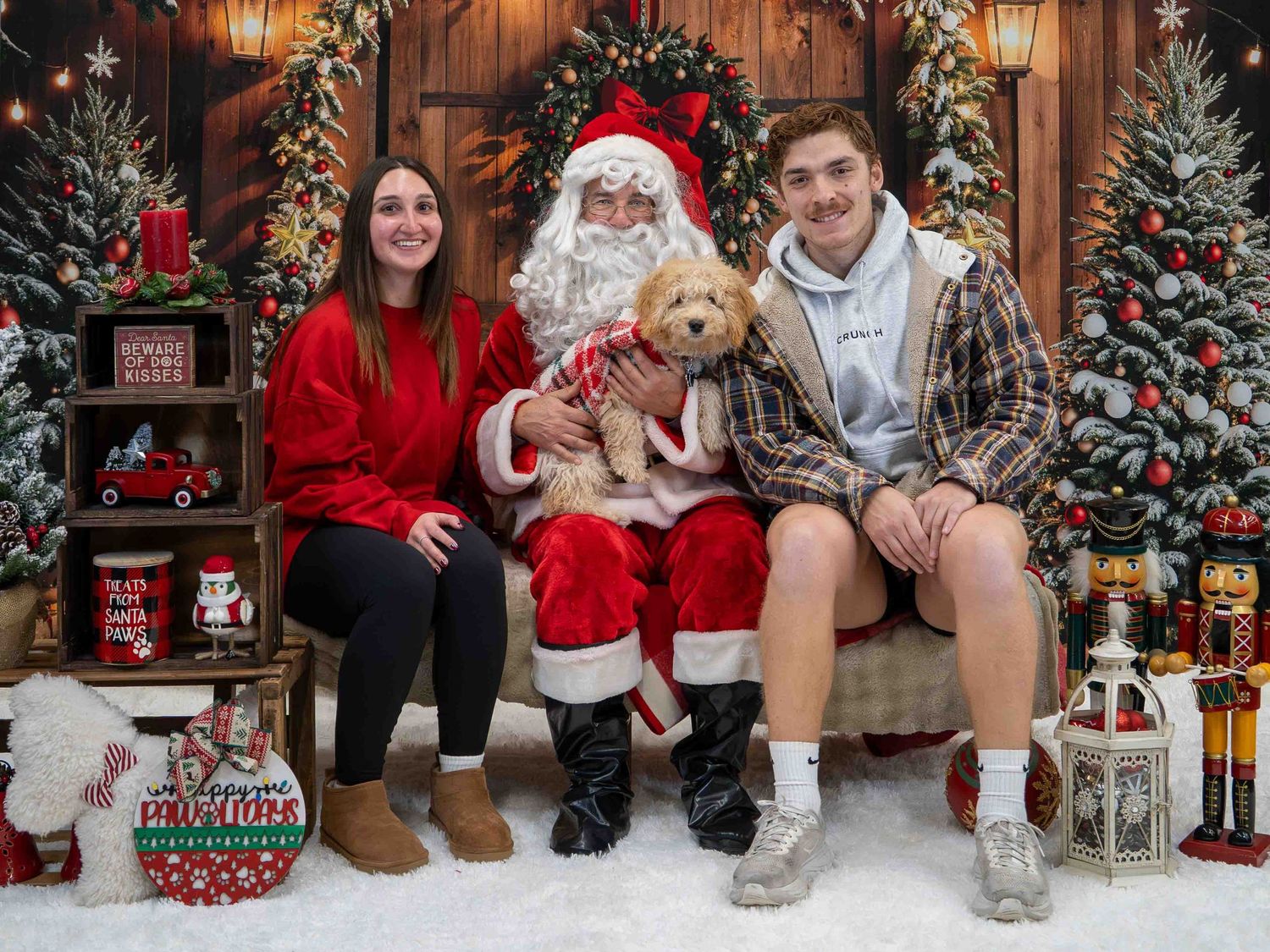 A couple poses with Santa Claus holding an adorable goldendoodle puppy in a decorated Christmas photo studio.