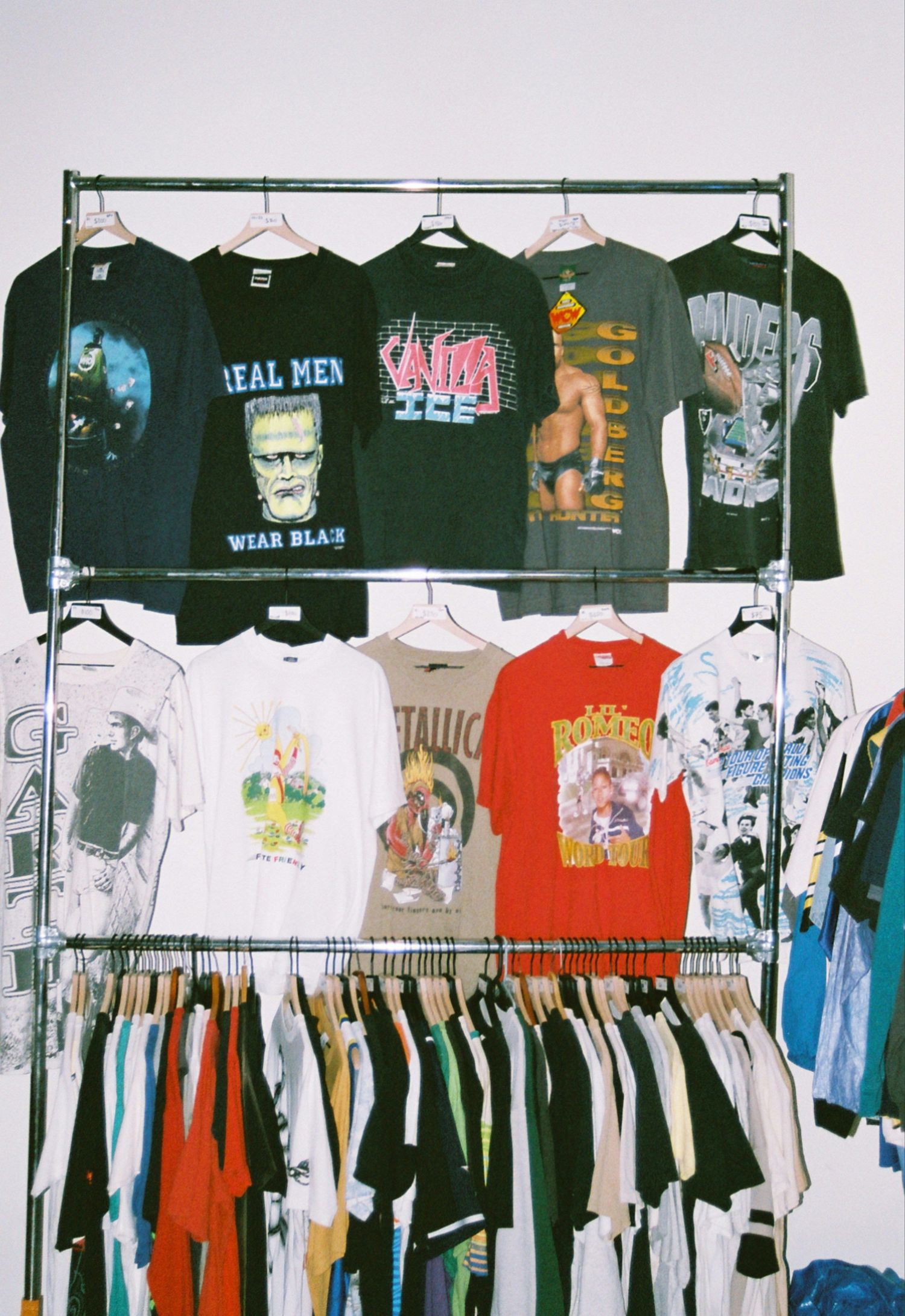Vintage graphic t-shirts displayed on a metal clothing rack, featuring band and pop culture designs in a retail shop setting.