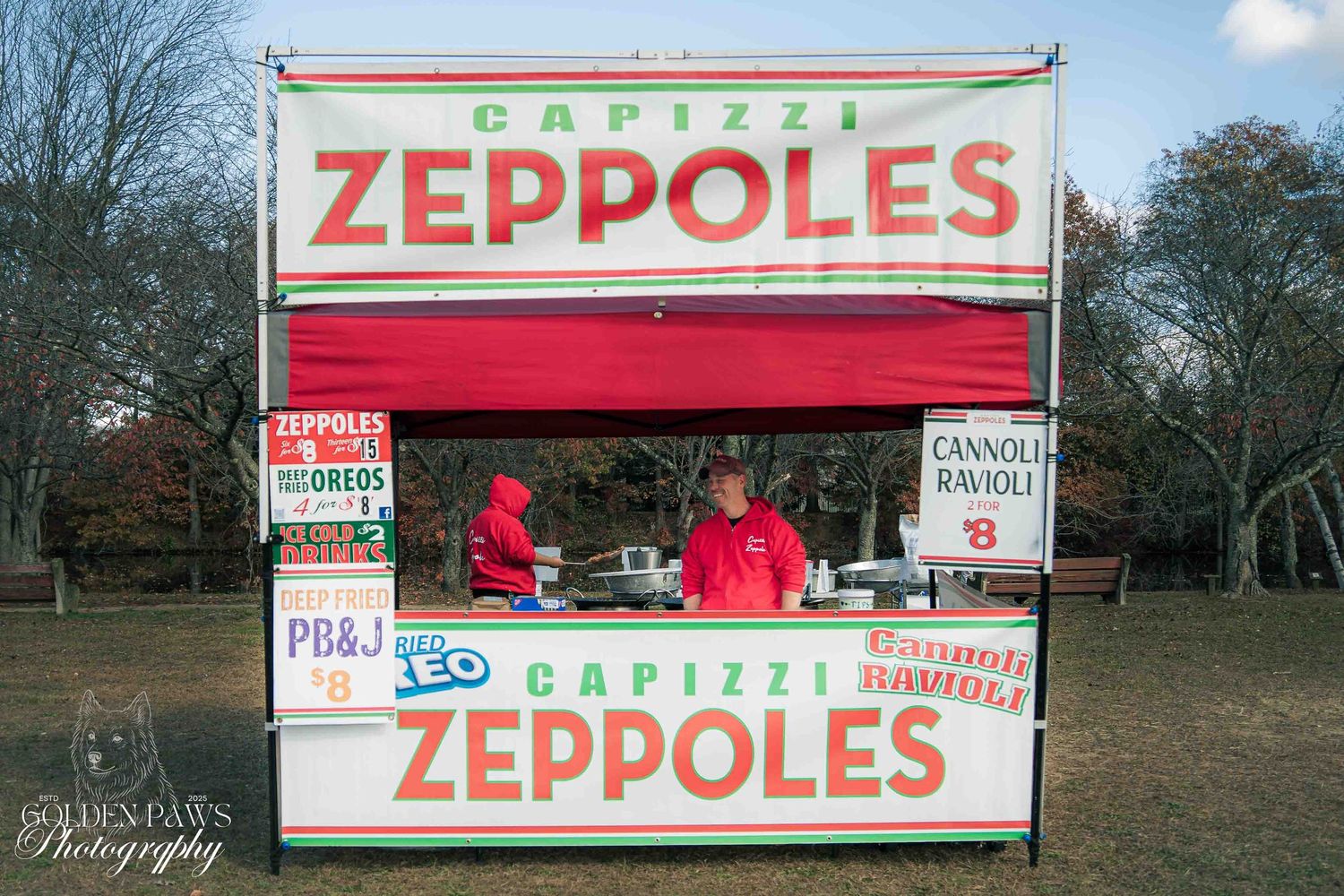 Capizzi Zeppoles food stand in a park with red and white signage and vendors in red shirts serving Italian treats.
