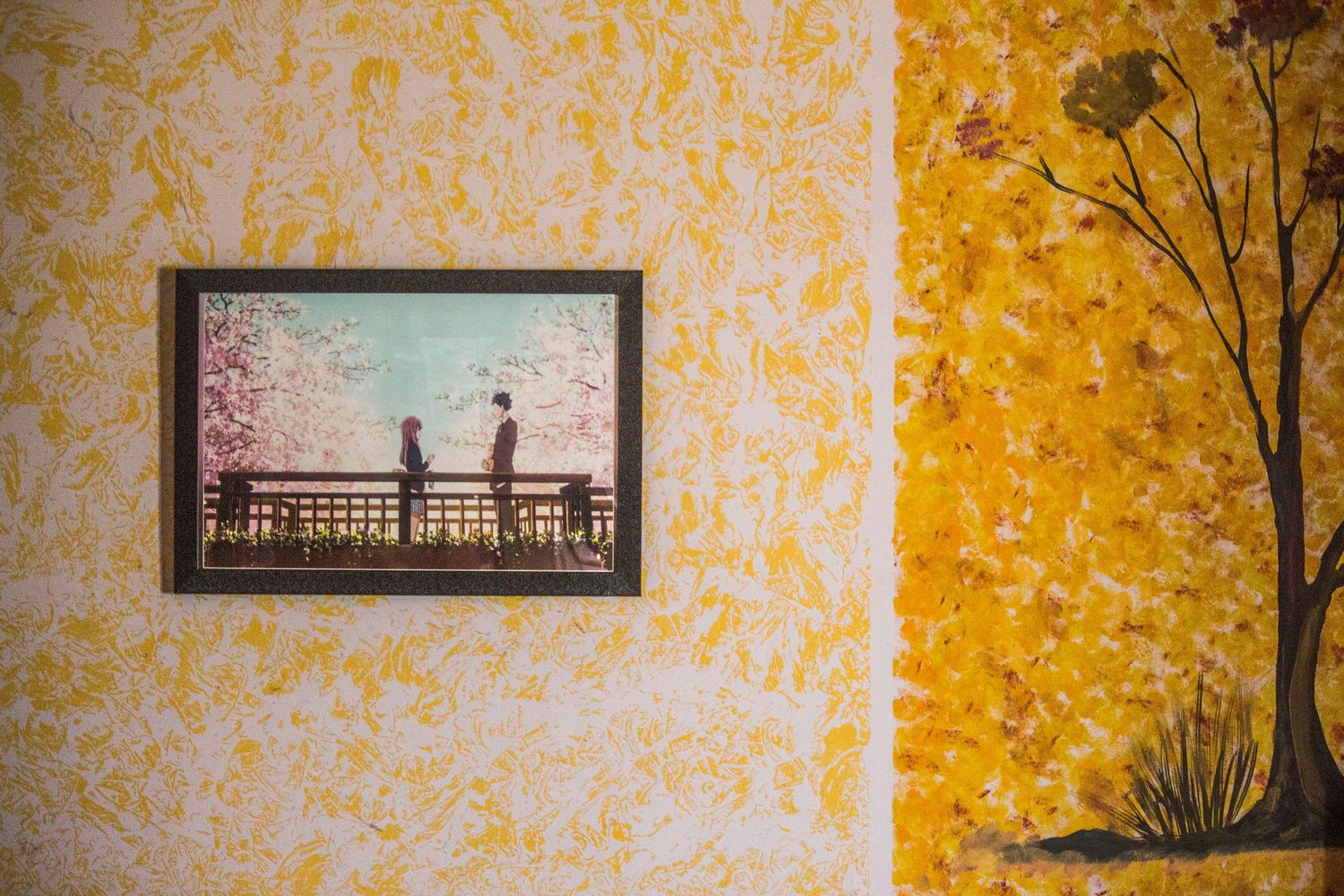 Framed anime artwork on yellow floral wallpaper beside a painted autumn tree mural.