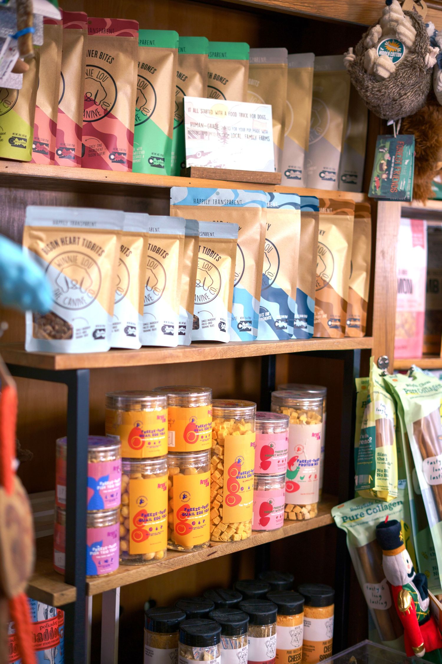 Wooden retail shelves displaying colorful packaged pet treats and jarred dog snacks in a store.