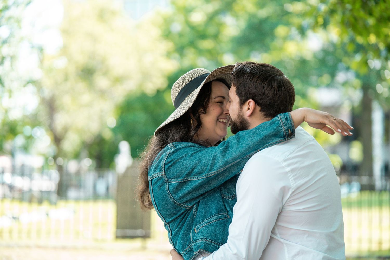 A happy couple embracing and smiling in a sunny park, woman wearing a hat and denim jacket. Worcester Common Oval