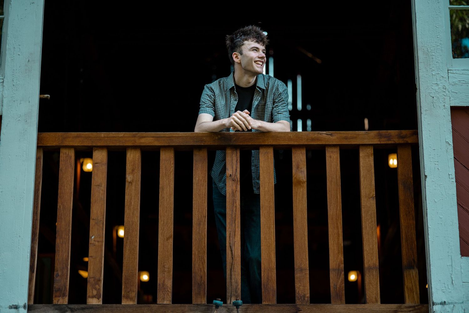 Young man leaning on a wooden railing of a rustic balcony, gazing thoughtfully into the distance at night.