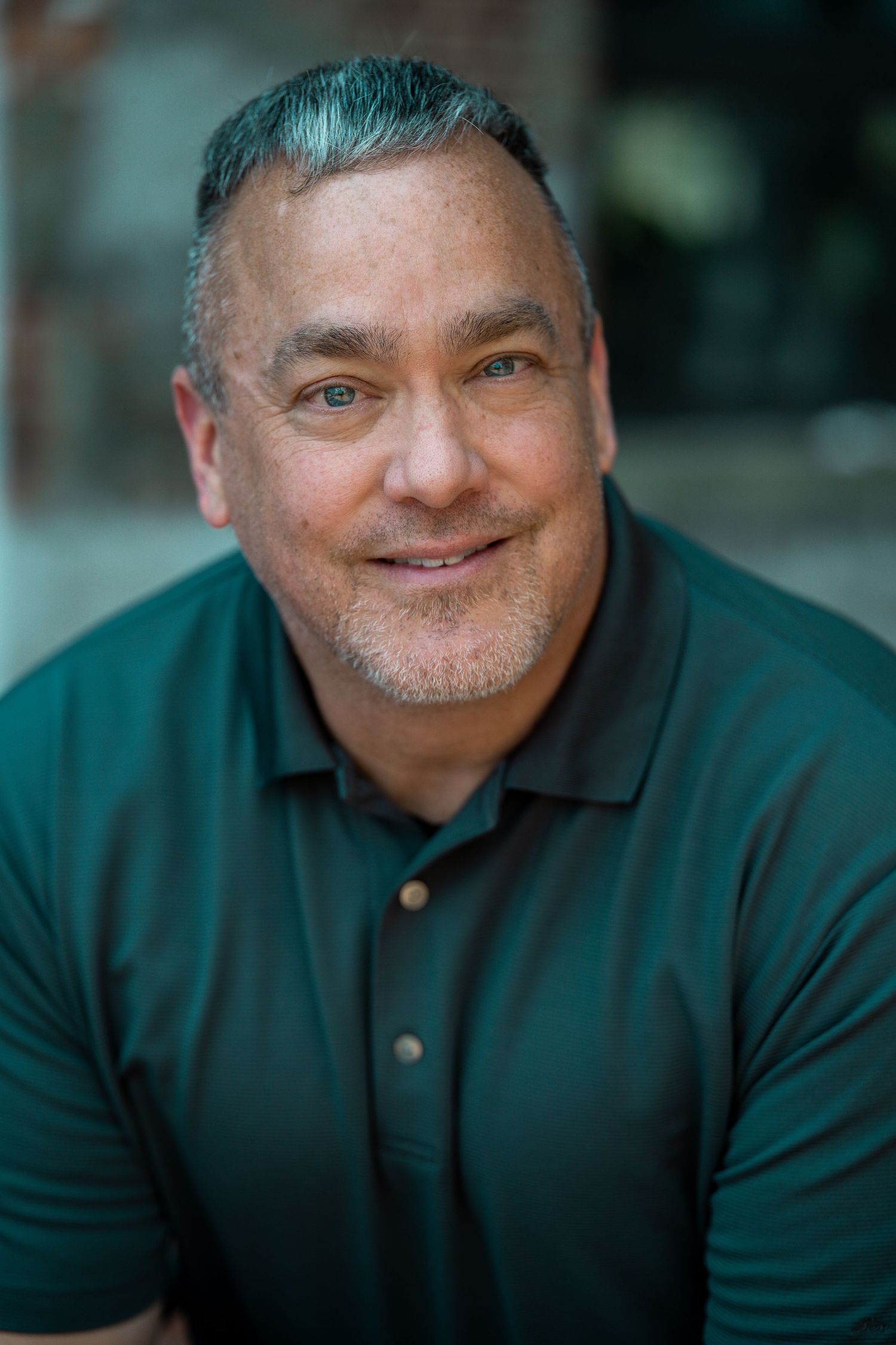 Smiling middle-aged man with salt-and-pepper hair wearing a dark green polo shirt in a professional headshot photo. Worcester MA headshot