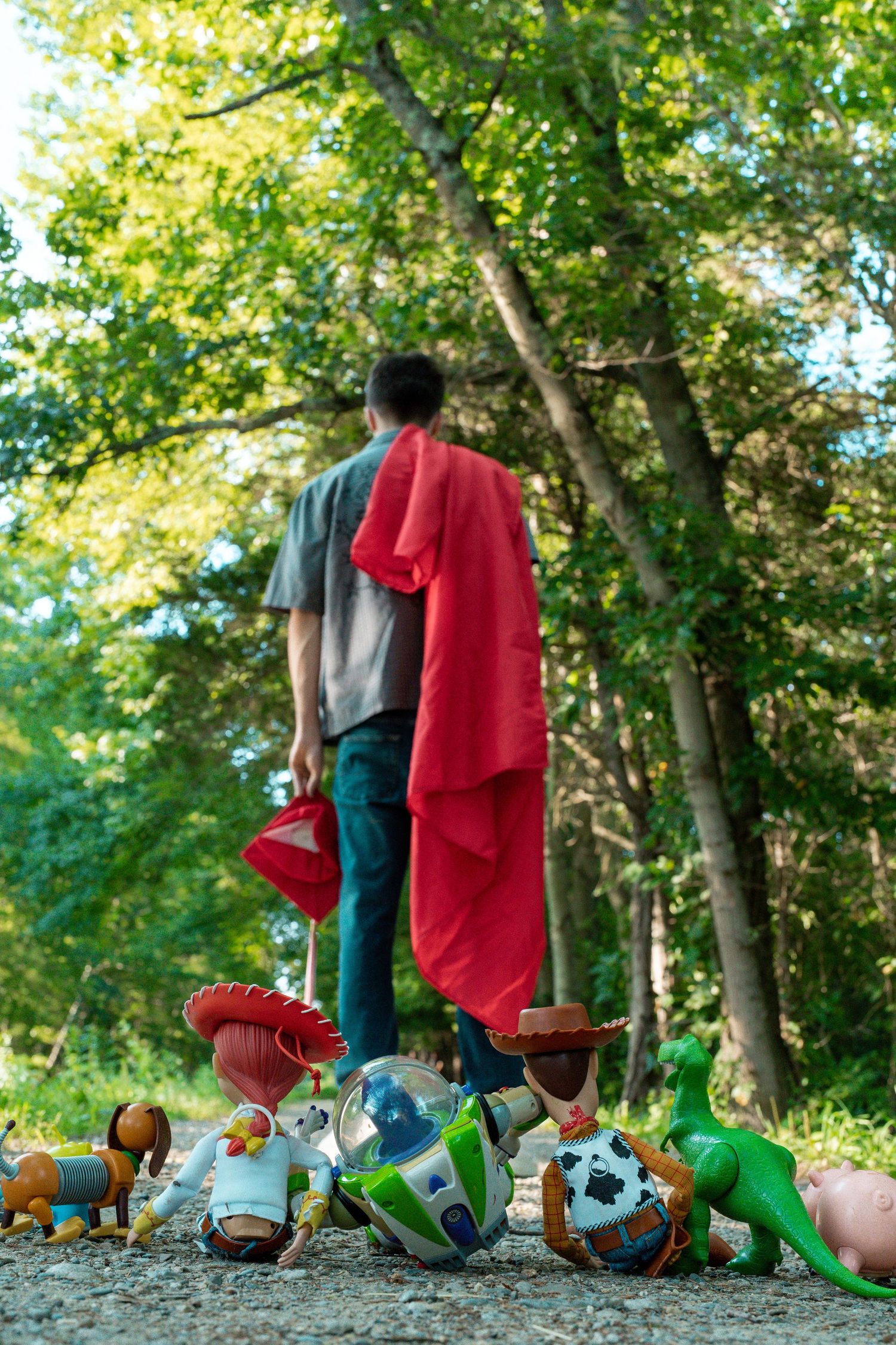 Man walking away from scattered Toy Story character toys including Woody, Buzz, and Jessie on a forest path.