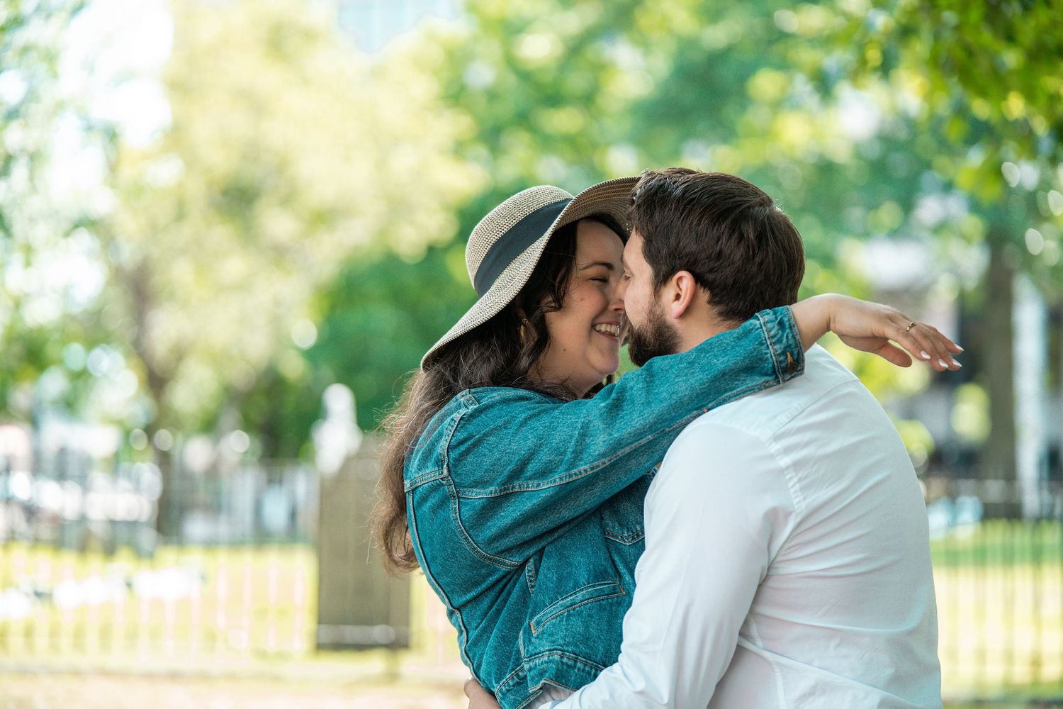 A happy couple embracing and smiling in a sunny park, woman wearing a hat and denim jacket. Worcester City Hall Common Oval.