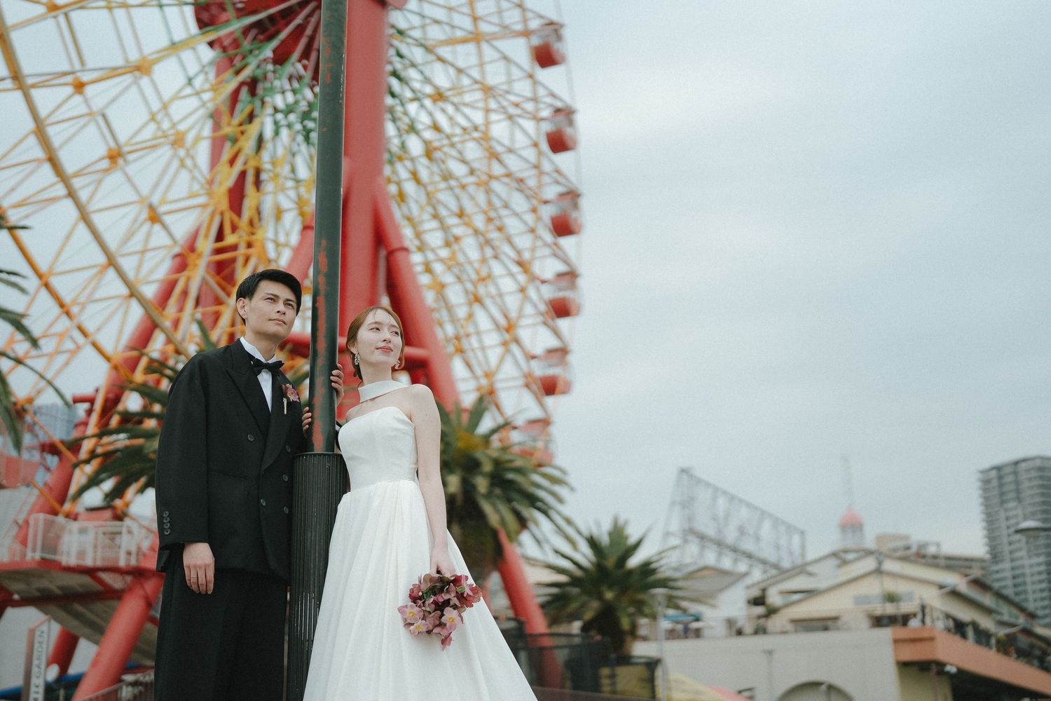 観覧車を背景に寄り添うご夫婦の晴れやかなウェディングフォト