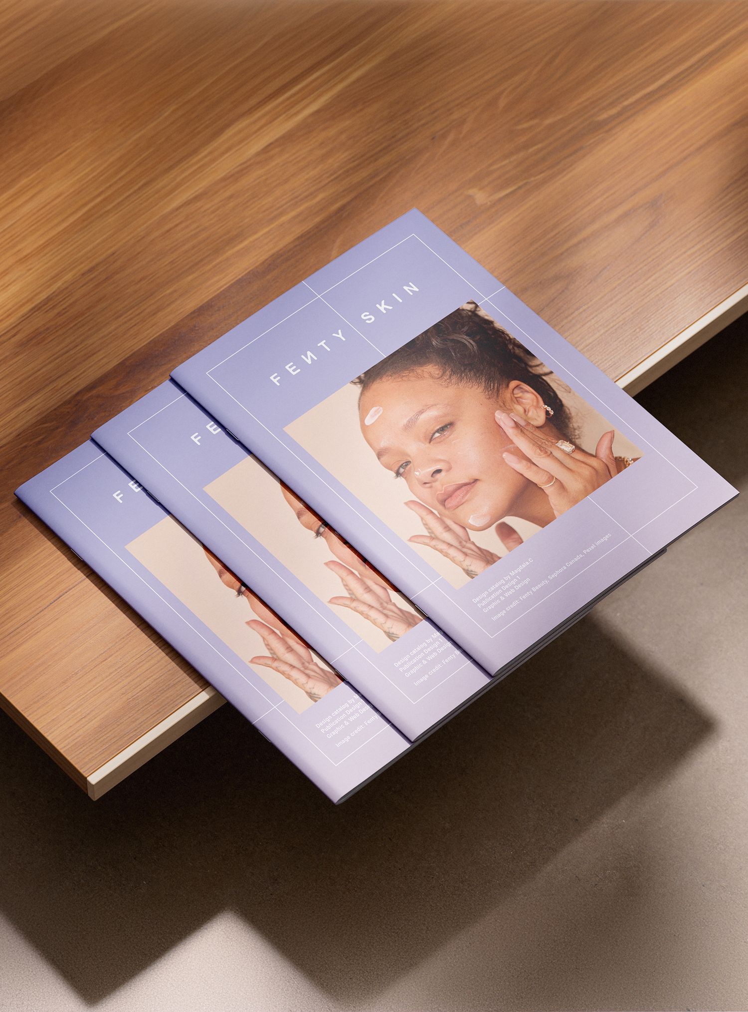 Three Fenty Skin branded booklets with lavender covers featuring a model, stacked on a wooden surface.