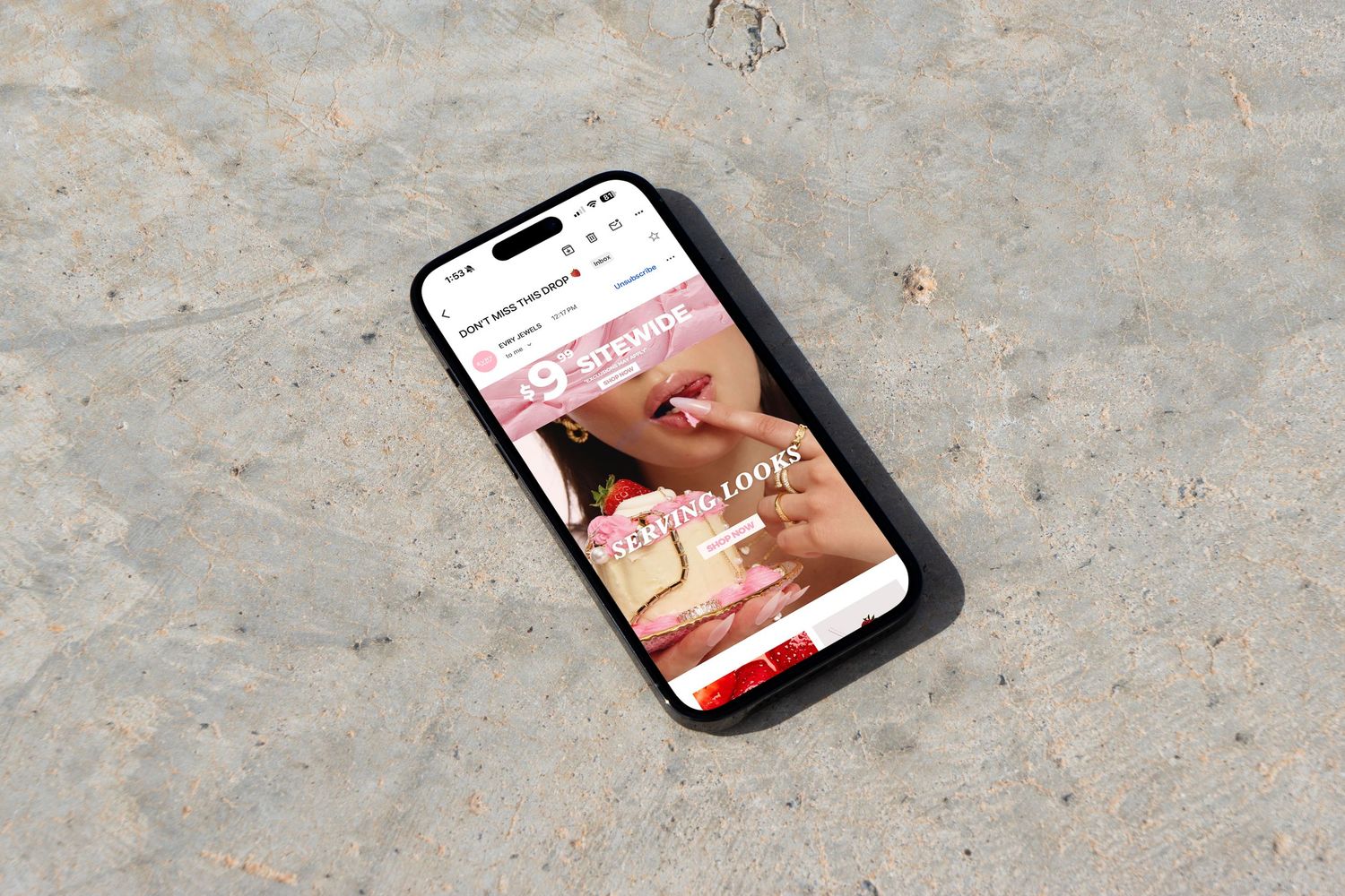 Mobile phone on sand displaying a pink beauty brand website with cosmetic product photography.
