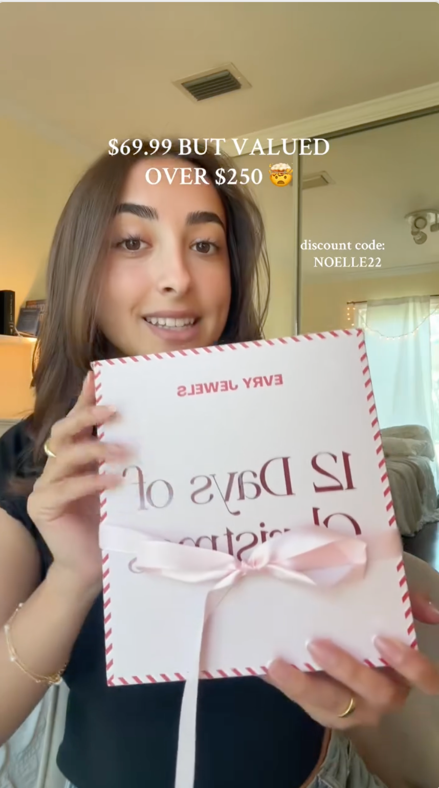 Woman holding Evry Jewels 12 Days of Christmas advent calendar valued over $250 with discount code NOELLE22.