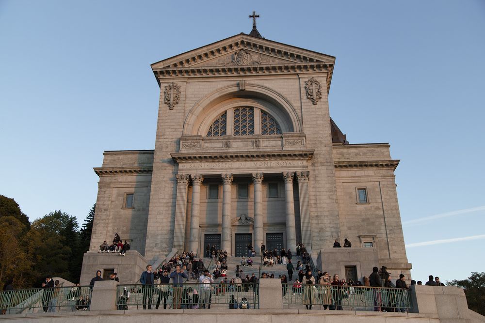 Large neoclassical stone church facade with crowd gathered on steps at dusk.