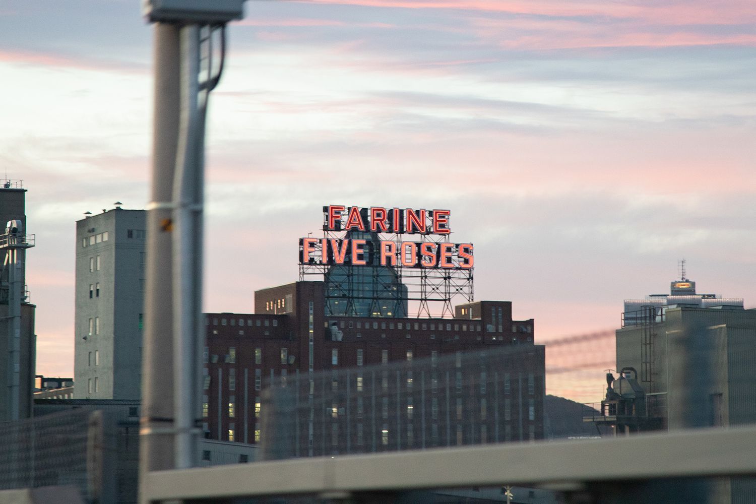 Farine Five Roses illuminated sign on Montreal building at dusk with pink and blue sky.