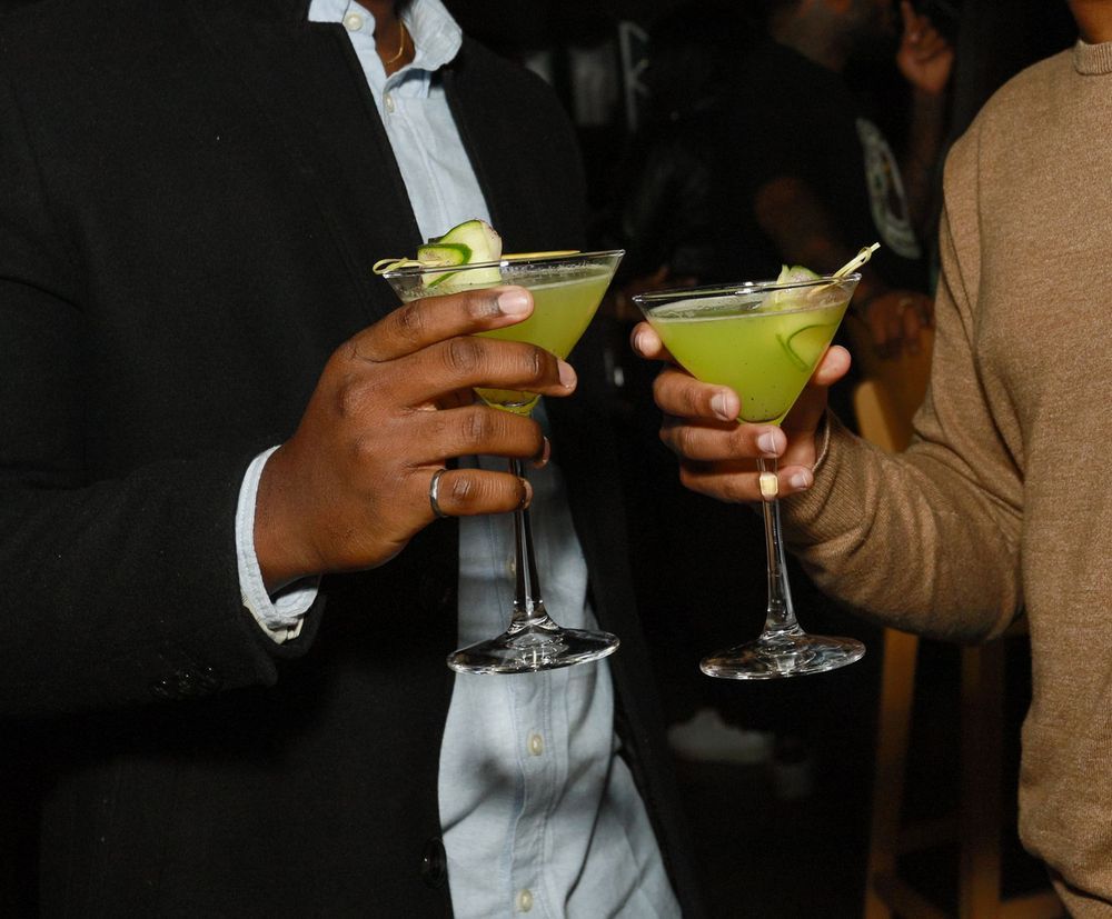 Two people clinking green martini cocktails garnished with lime at a social gathering event.