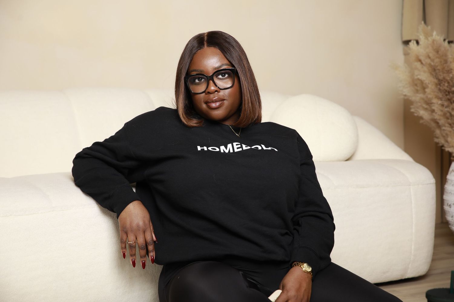 Woman in black Homebody sweatshirt sitting on white couch in cozy home setting.