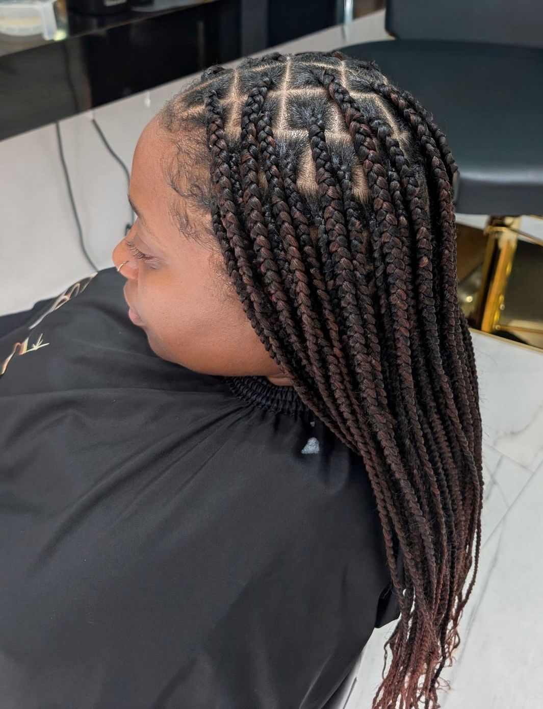 Person wearing black cape with dark brown box braids styled with clean parts at a hair salon.