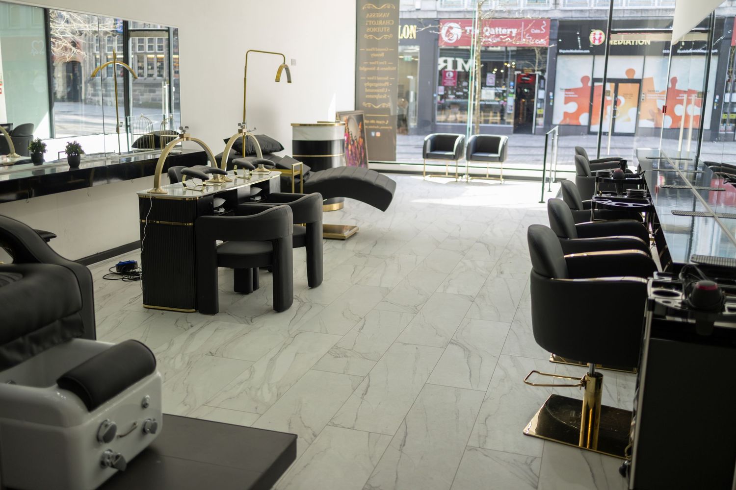Modern hair salon interior with black styling chairs, marble floors, and large windows offering a bright, luxurious space.