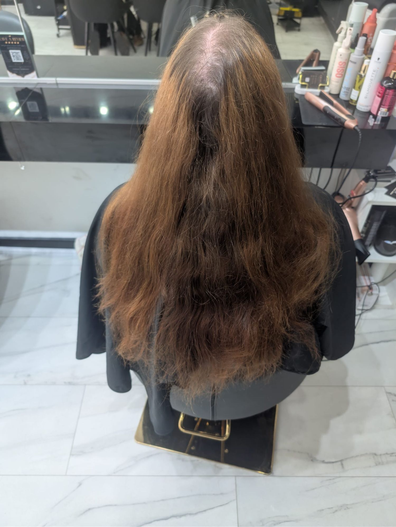 Back view of long brown hair with visible thinning at crown, shown in a salon setting before treatment.