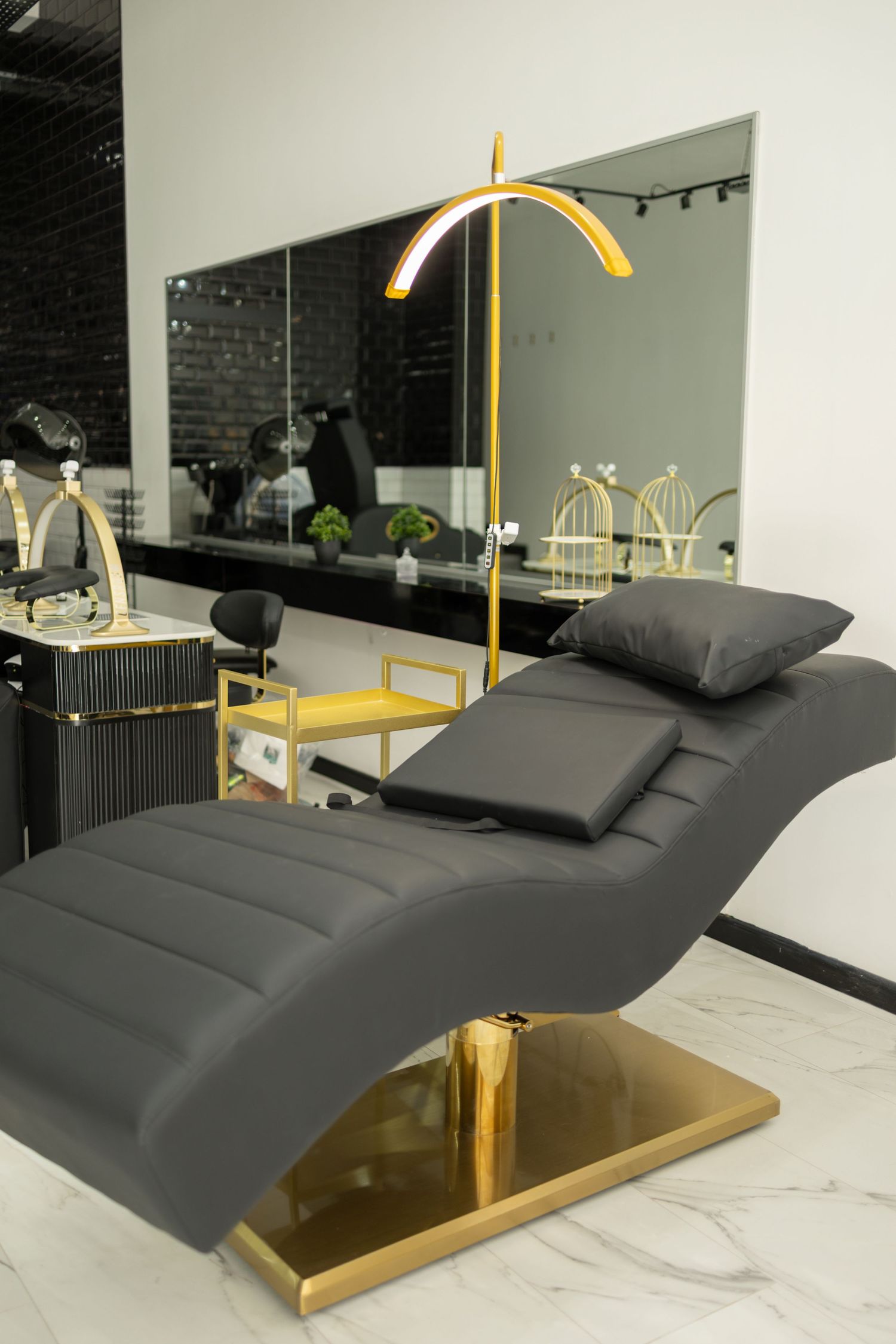 Luxurious black leather salon chair with gold base and lamp, marble floor, and mirrored vanity in modern beauty studio.