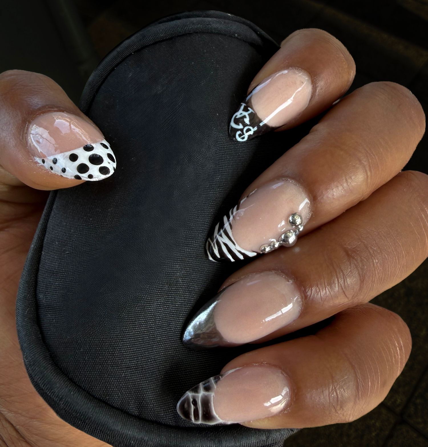 Stiletto nails with black and white animal print, zebra stripes, rhinestones, and silver French tips on dark skin.
