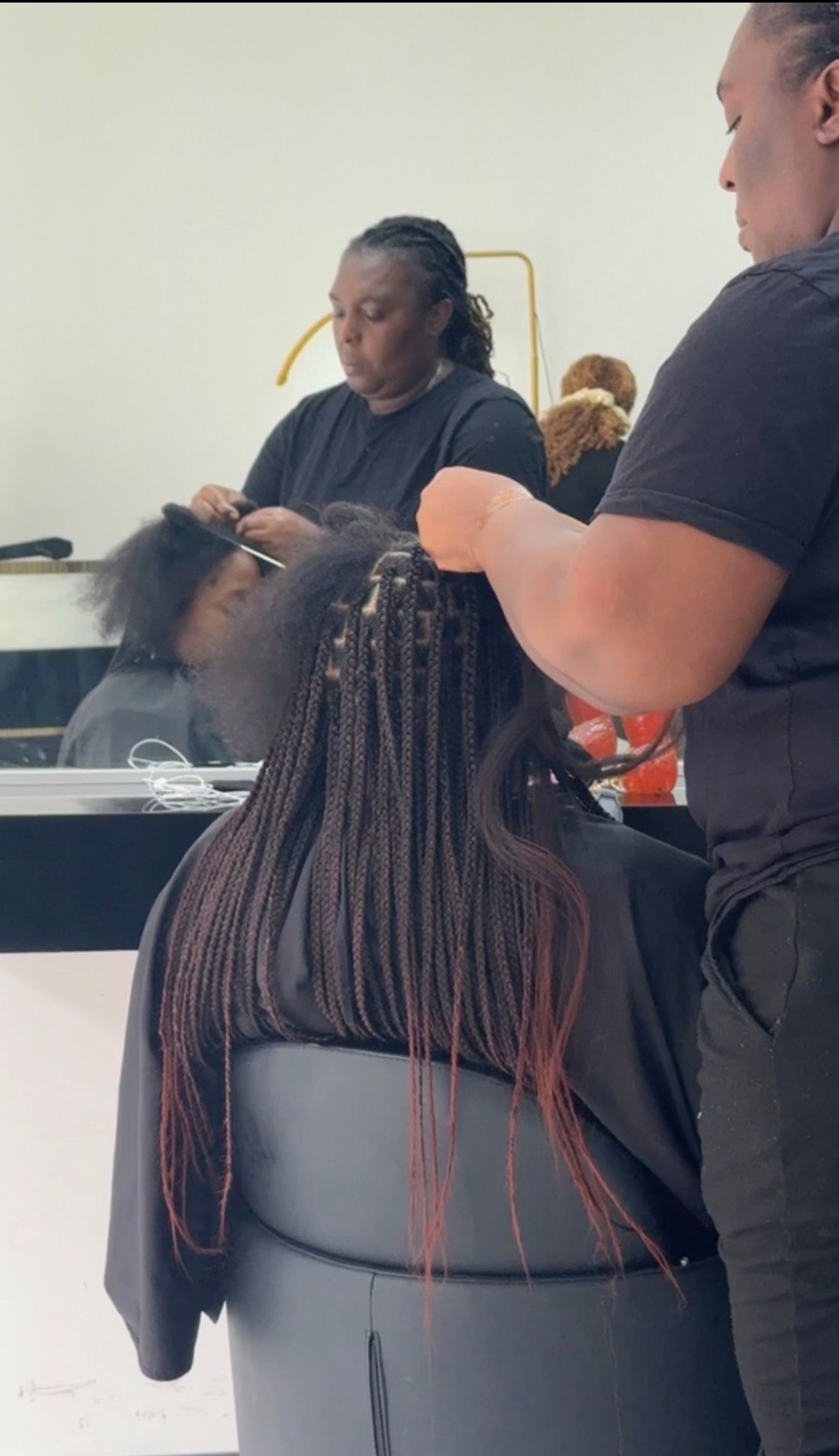 Hair stylist braiding long dark red-tipped box braids on a client in a modern salon.