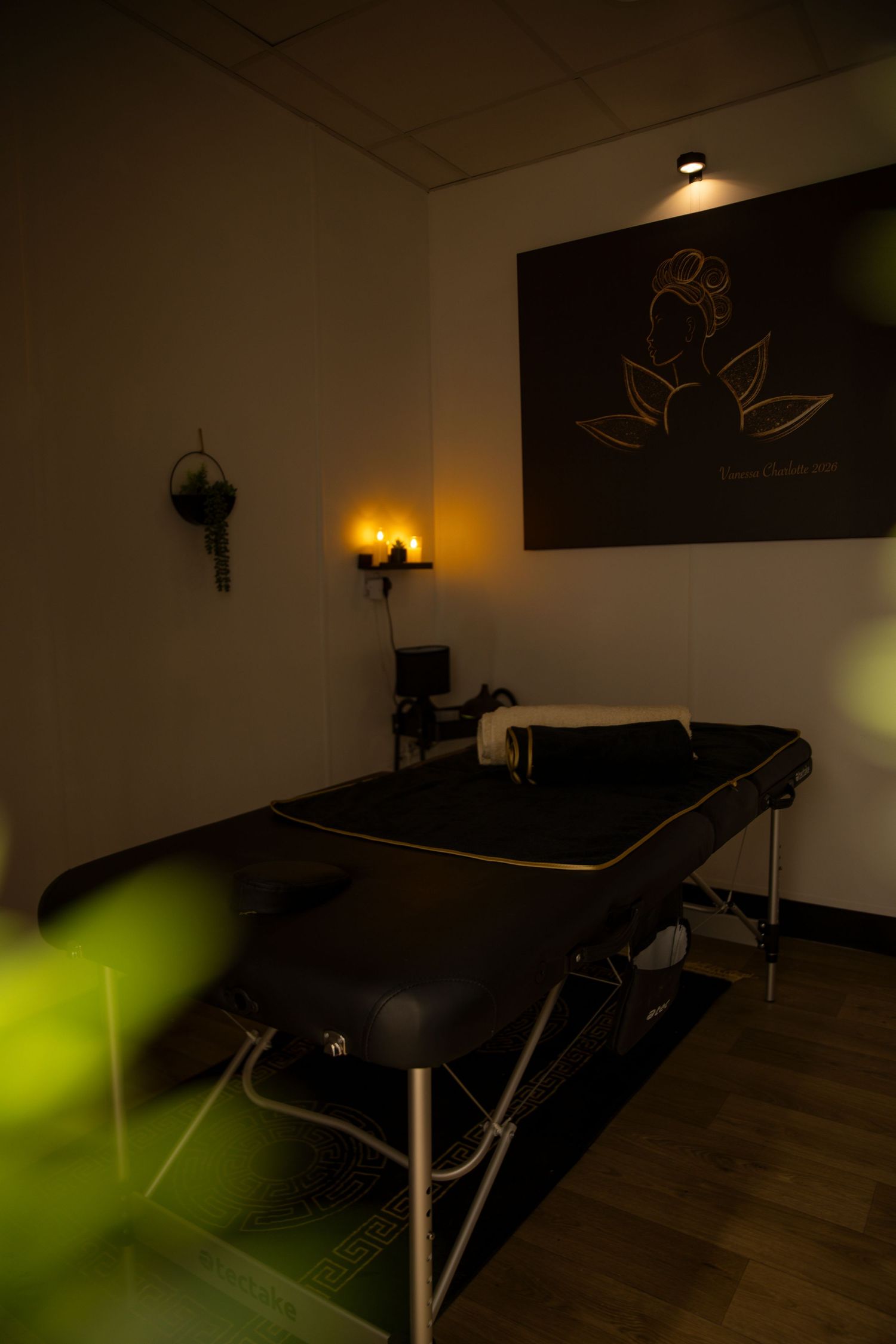 Dimly lit massage therapy room with black treatment table, warm ambient lighting, and lotus flower wall art.