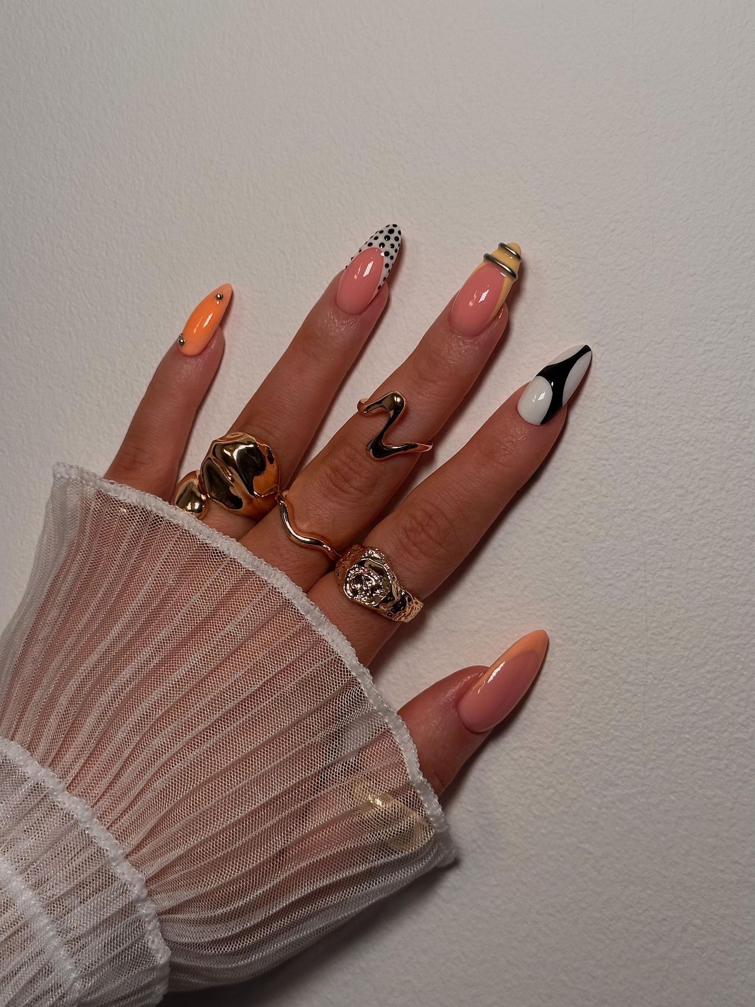 Close-up of almond-shaped nails with orange, black, white, and rhinestone nail art designs. Vanessa Charlotte Studios Wolverhampton