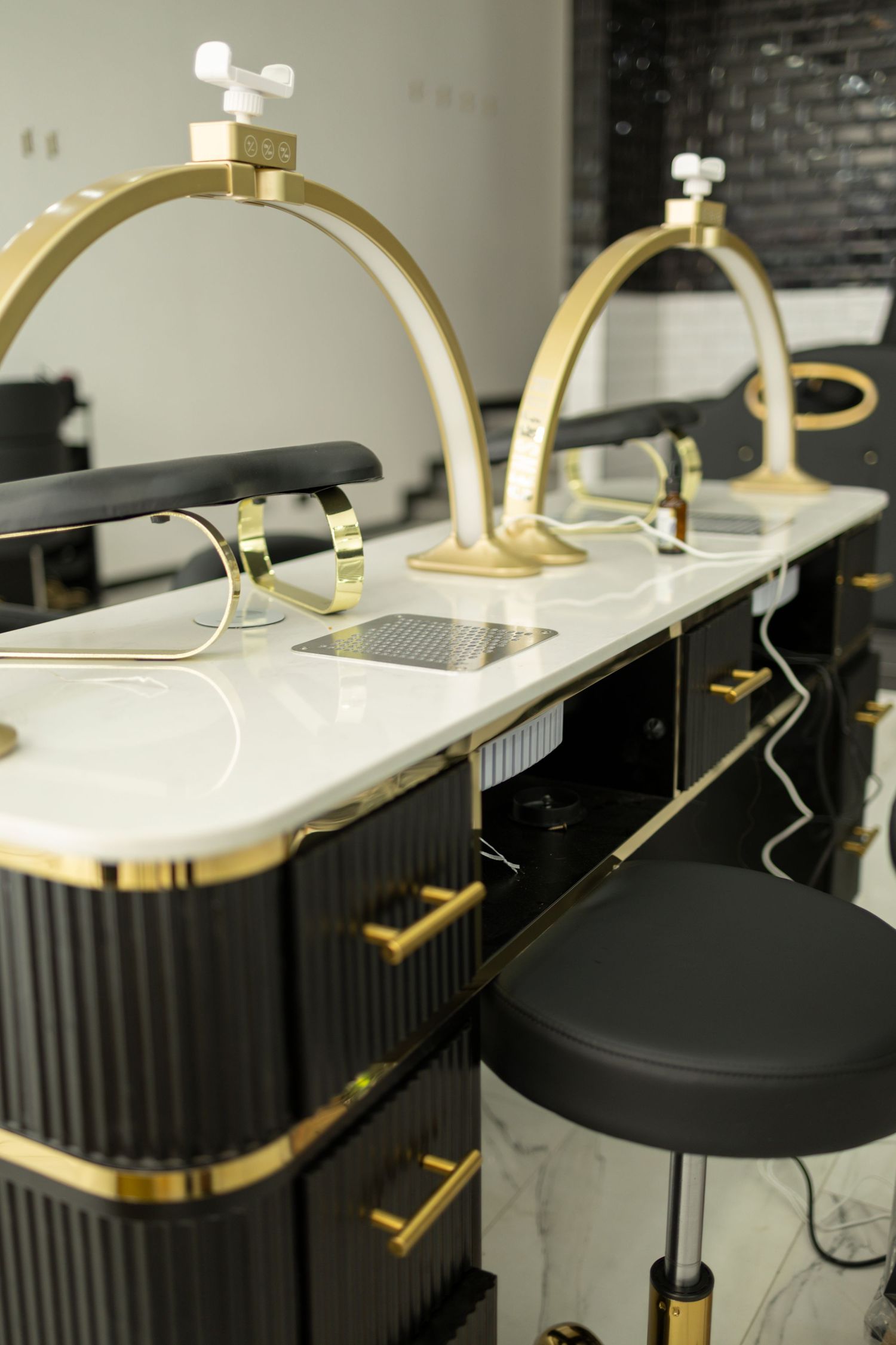 Luxury nail salon manicure stations with black and gold accents, marble countertops, and arch-shaped LED lamps.