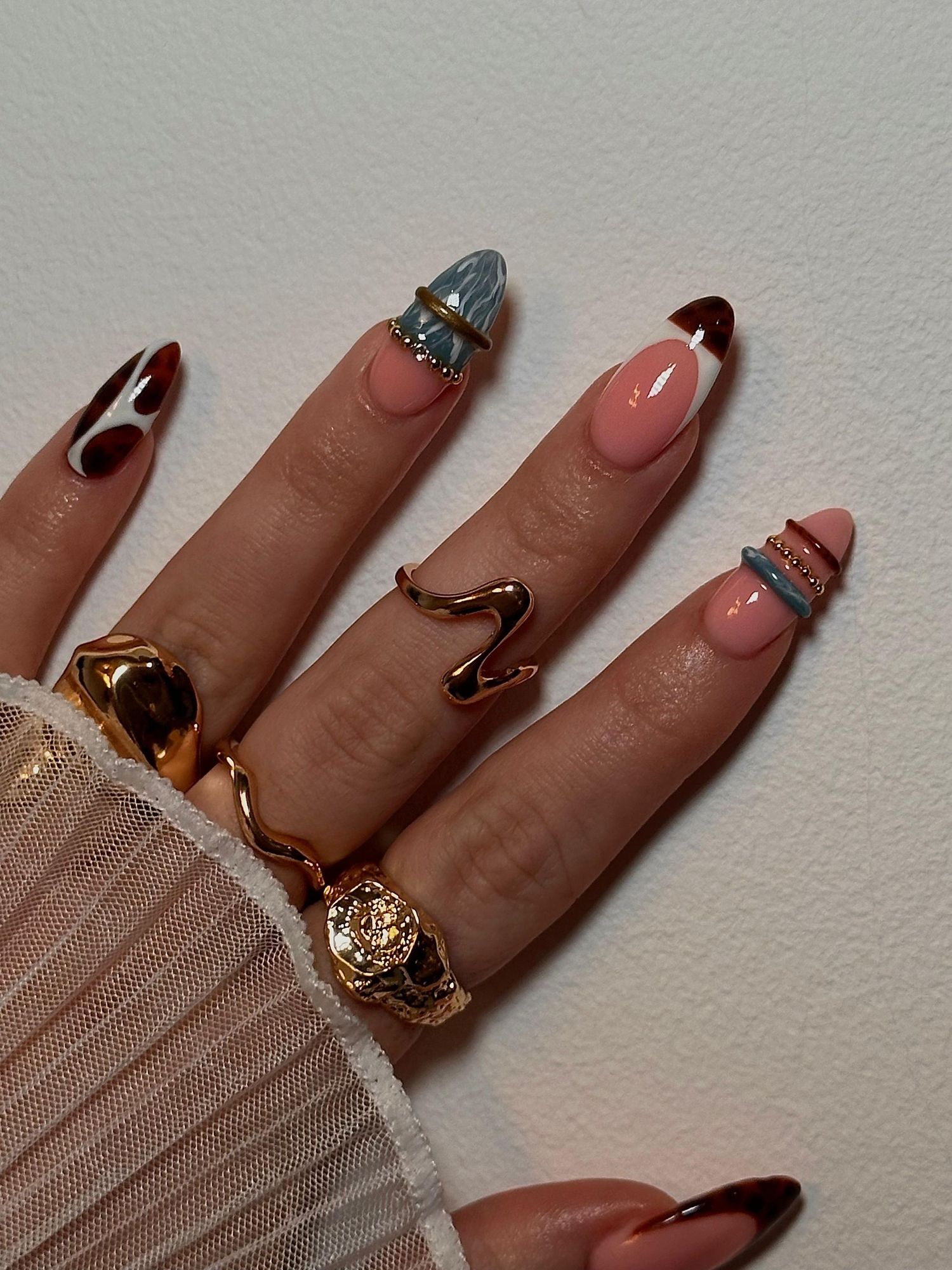 Hand with artistic mixed almond nails featuring cow print, chrome, and nude tones with gold rings. Vanessa Charlotte Studios Wolverhampton