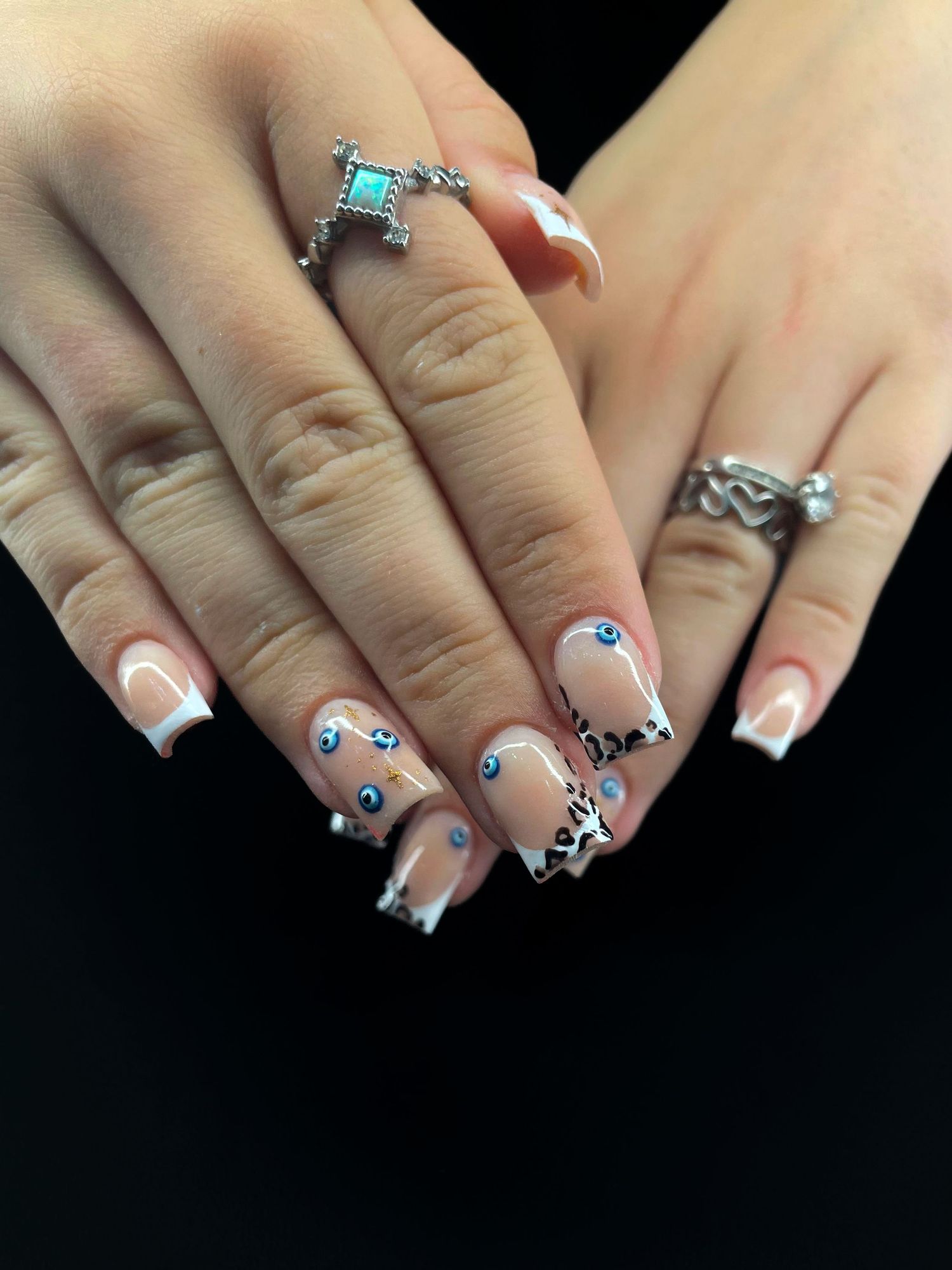 French tip nails with evil eye and floral designs, silver chrome accents, worn with turquoise cross and wave rings.