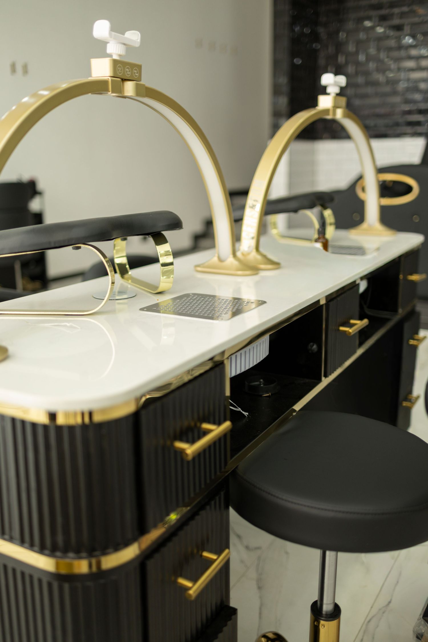 Luxury nail salon manicure stations with black and gold accents, marble countertops, and elegant arch-shaped lamp fixtures.