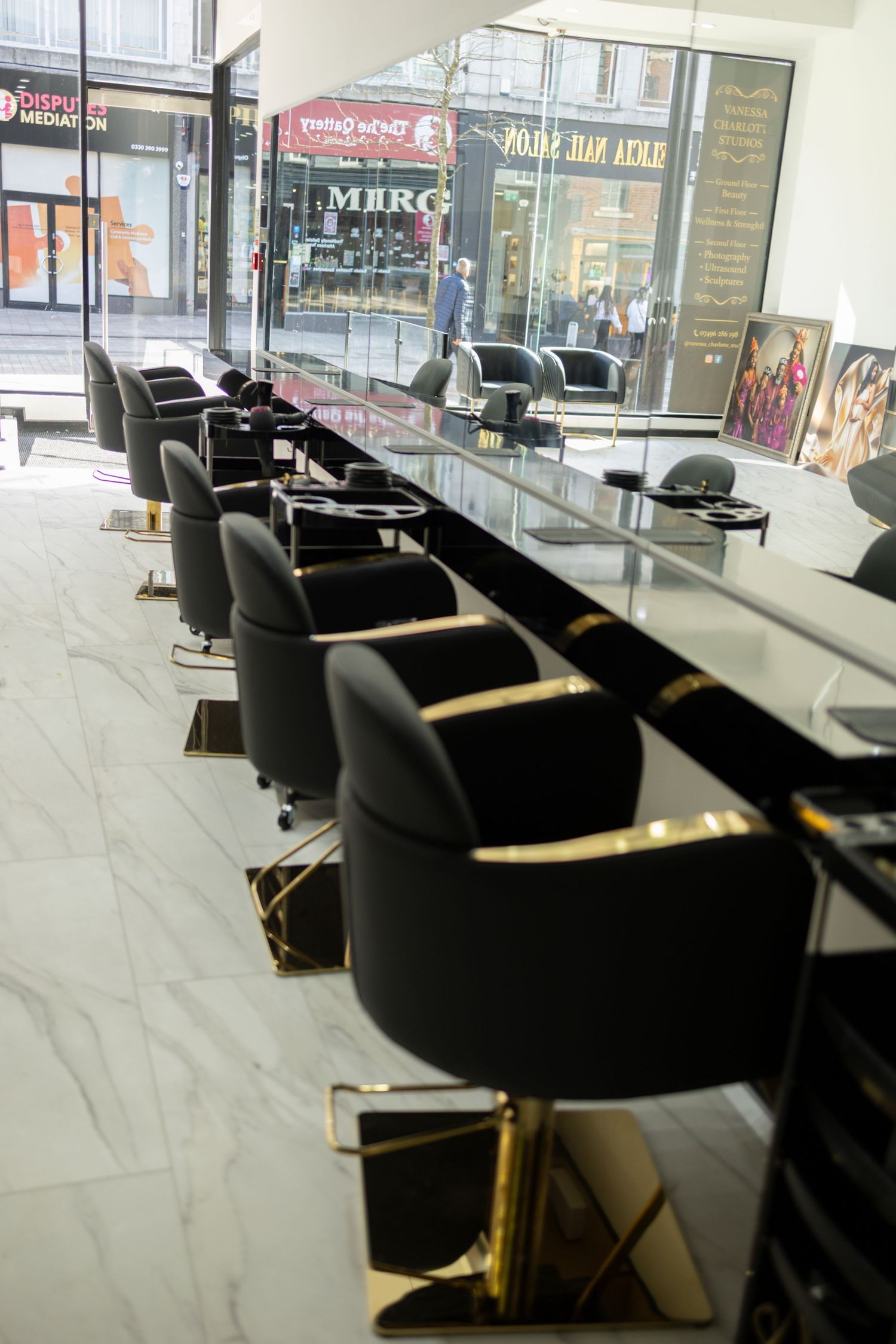Modern hair salon interior with black and gold styling chairs lined along a mirrored vanity counter on marble floors.