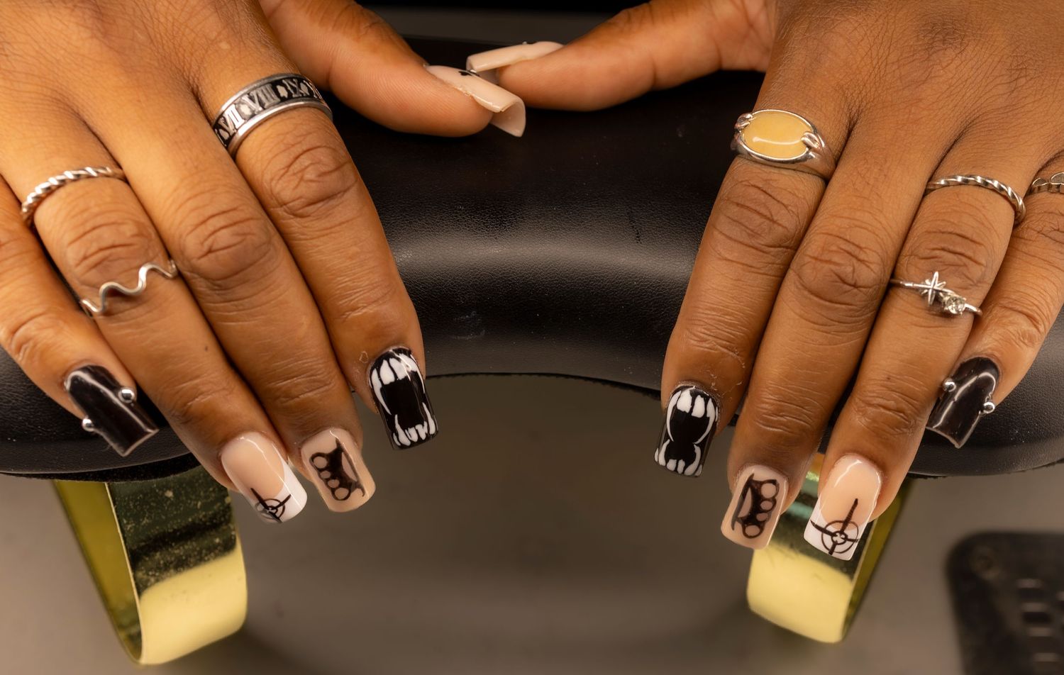 Close-up of square acrylic nails featuring black and nude Halloween nail art with spooky designs and silver rings.