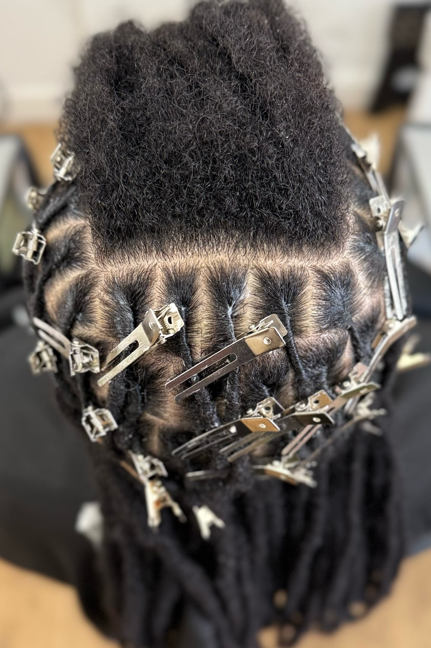 Close-up of natural Black hair sectioned with metal clips for loc retwist styling service.