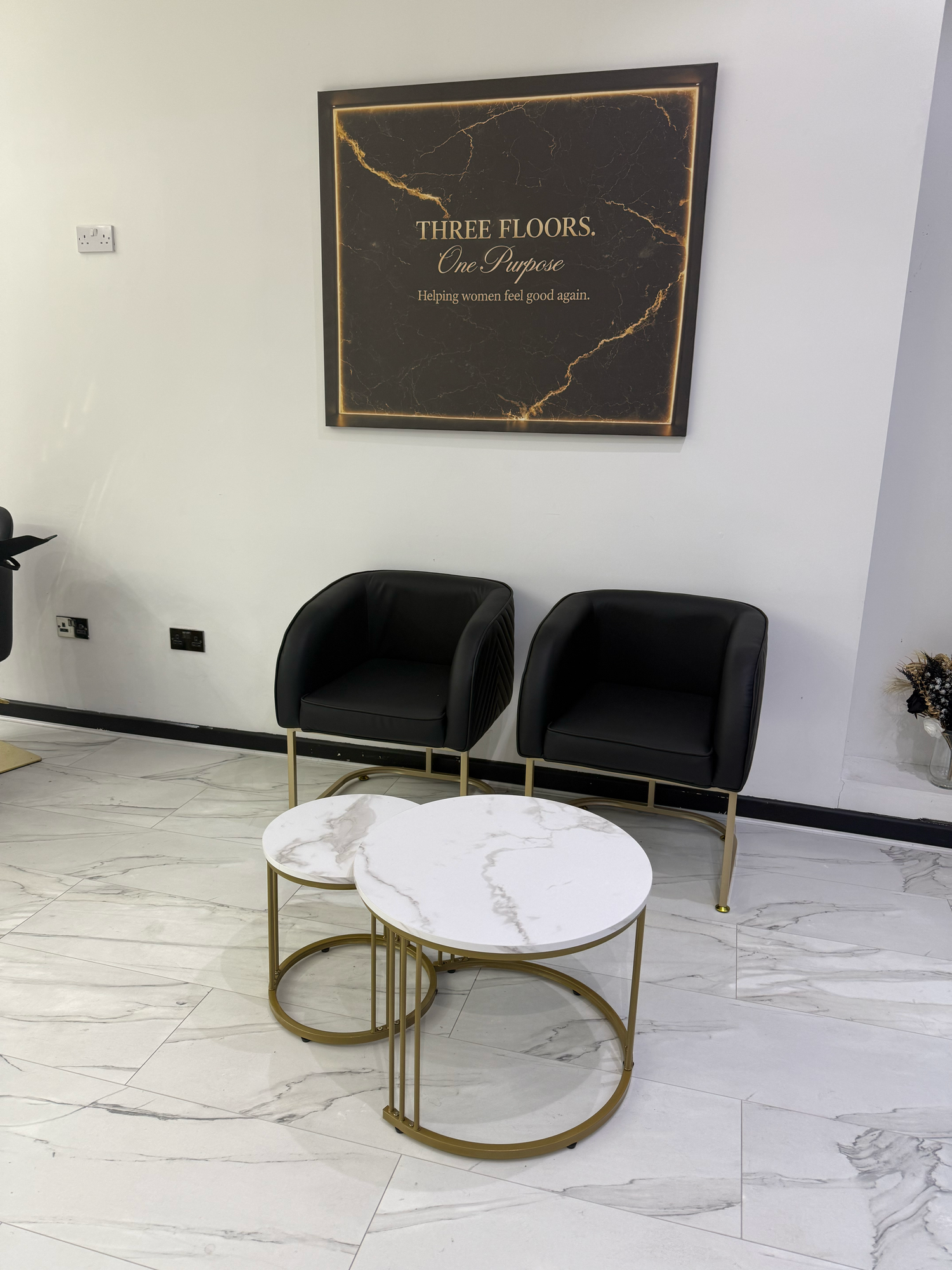 Modern waiting area with black velvet chairs, gold marble coffee table, and Three Floors One Purpose sign on white wall.