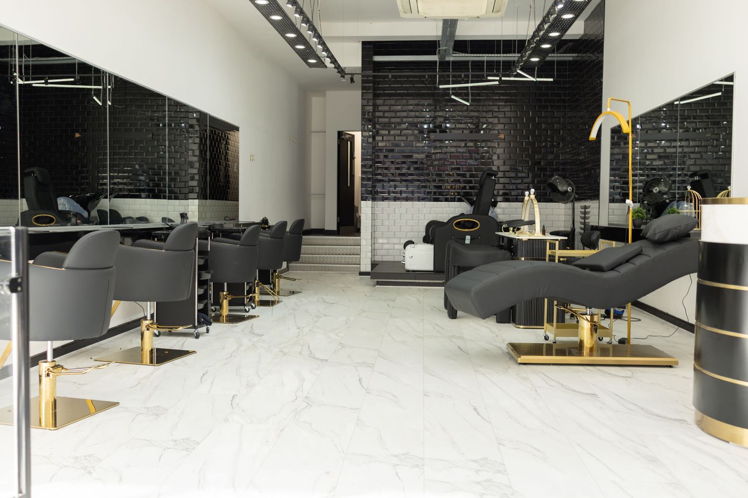 Modern hair salon interior with black chairs, gold accents, marble floors, and brick accent wall.