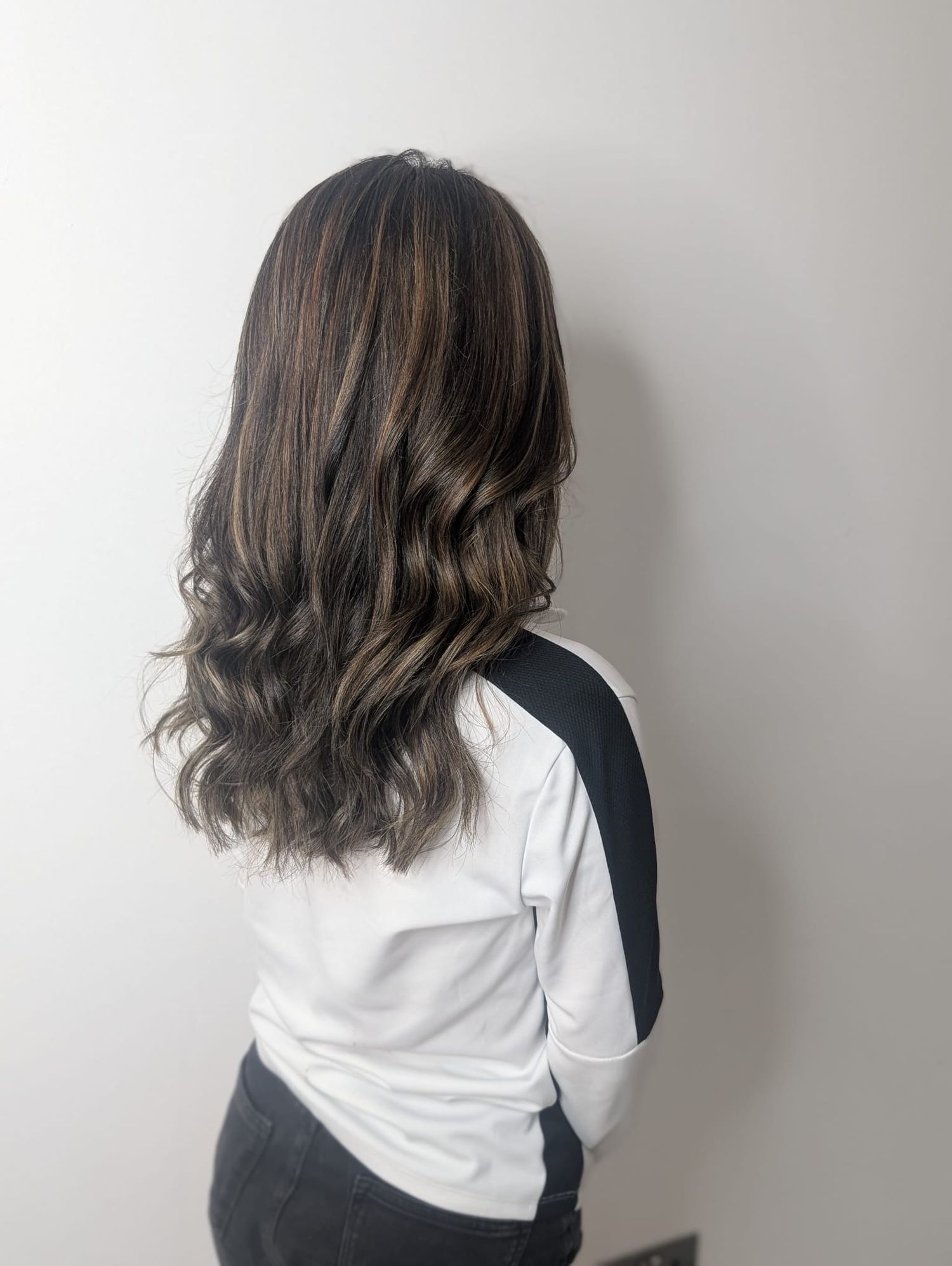 Back view of long dark brown wavy hair with subtle highlights, worn by a person in a white top.