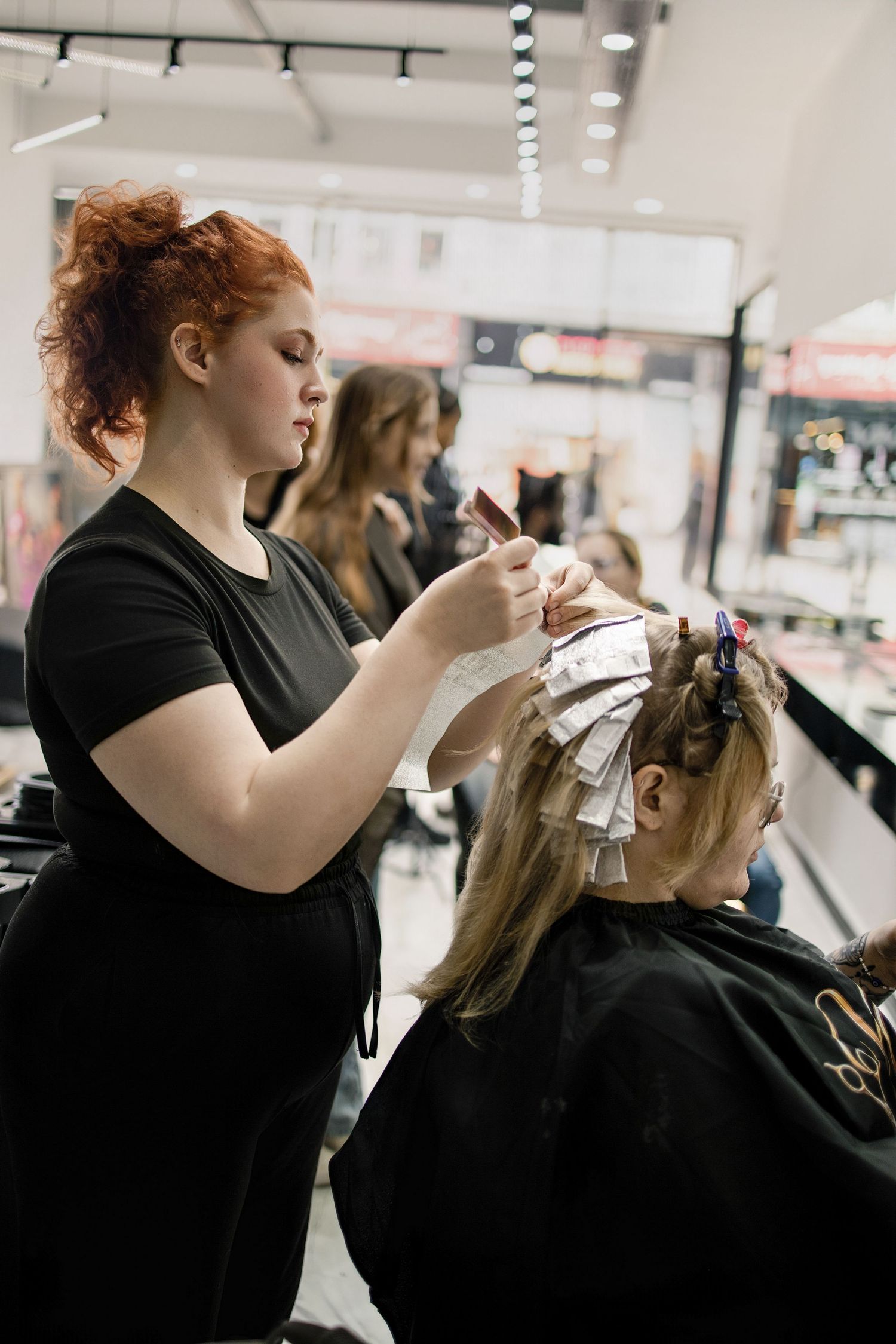 Red-haired stylist applying hair color treatment to a blonde client in a modern salon. Vanessa Charlotte Studios Wolverhampton