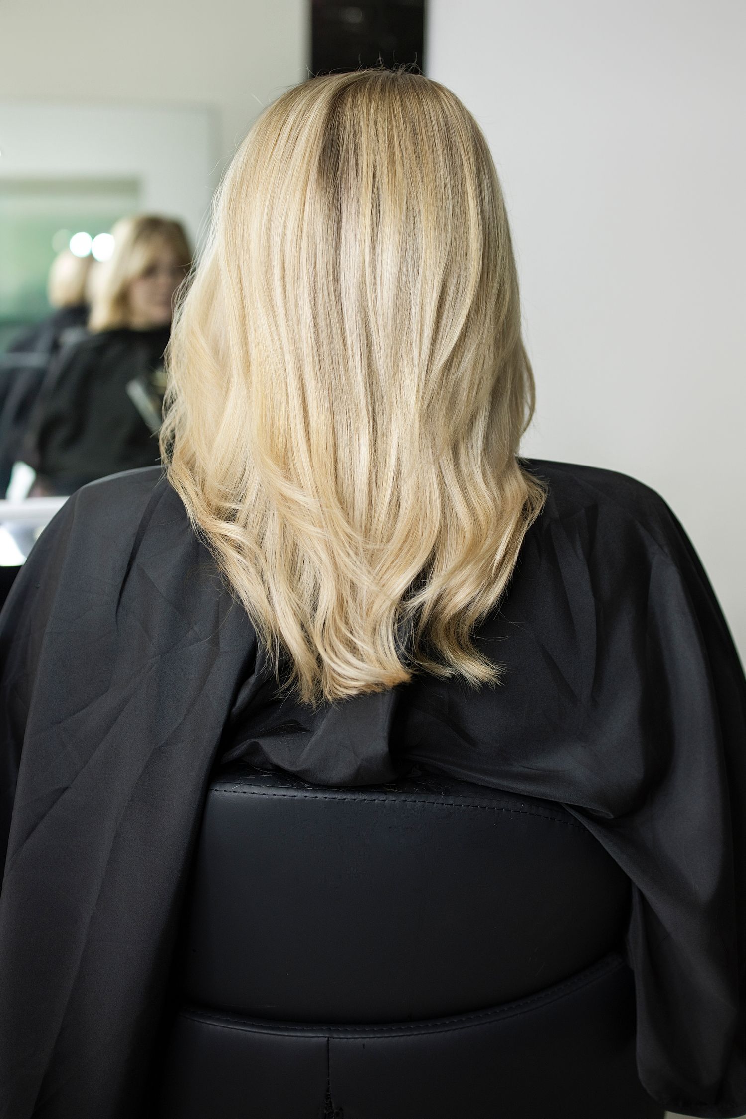 Back view of a woman with voluminous blonde wavy hair wearing a black salon cape. Vanessa Charlotte Studios Wolverhampton