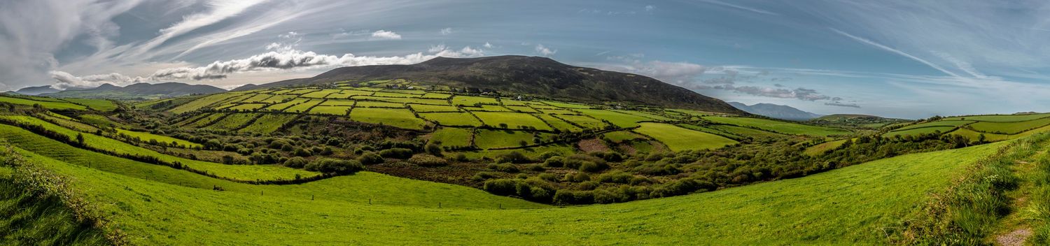 Panoramic view of lush green Irish countryside with rolling hills and mountains under a cloudy sky.