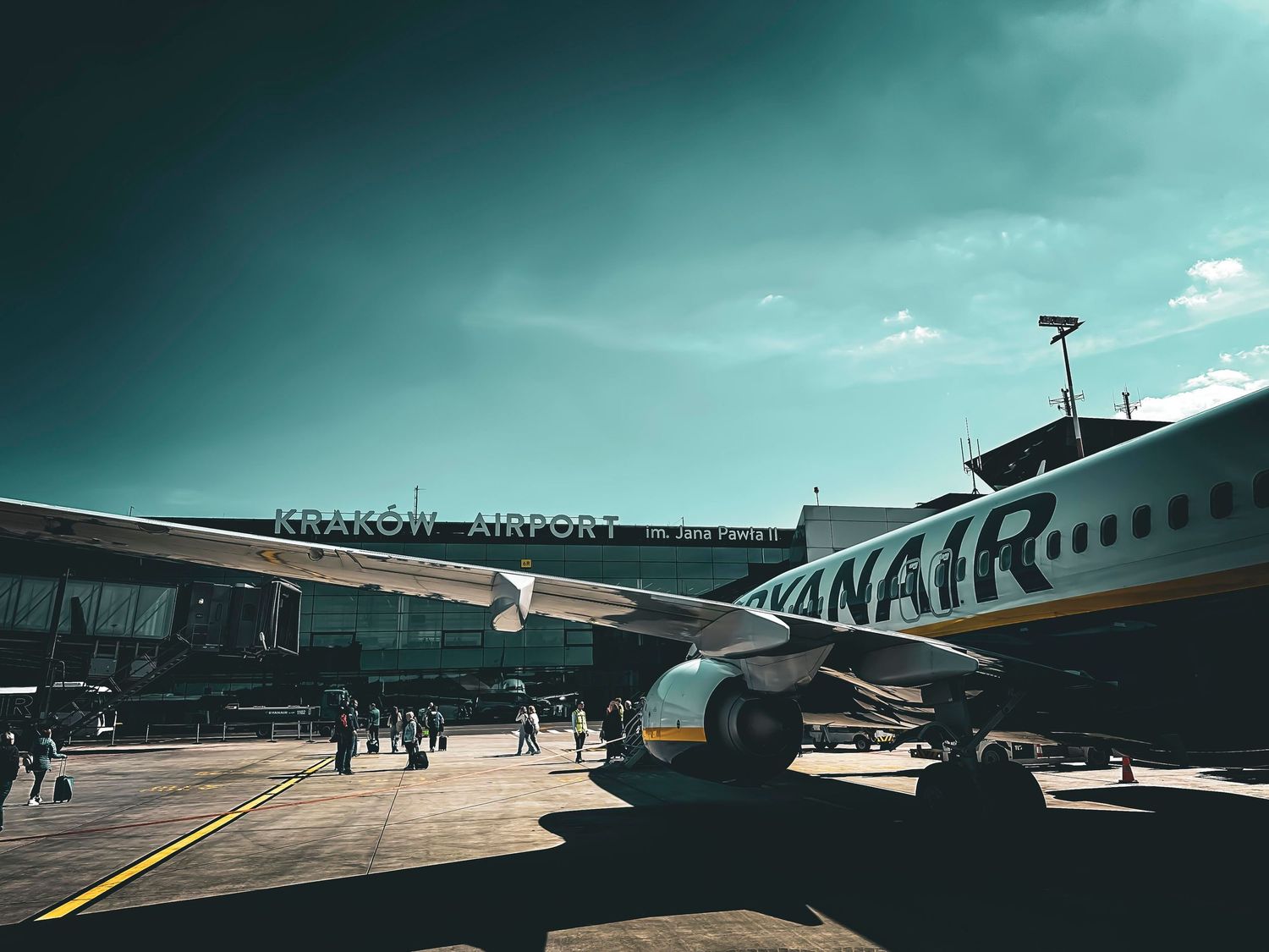 Ryanair aircraft at Krakow Airport gate with passengers boarding under dramatic sky.