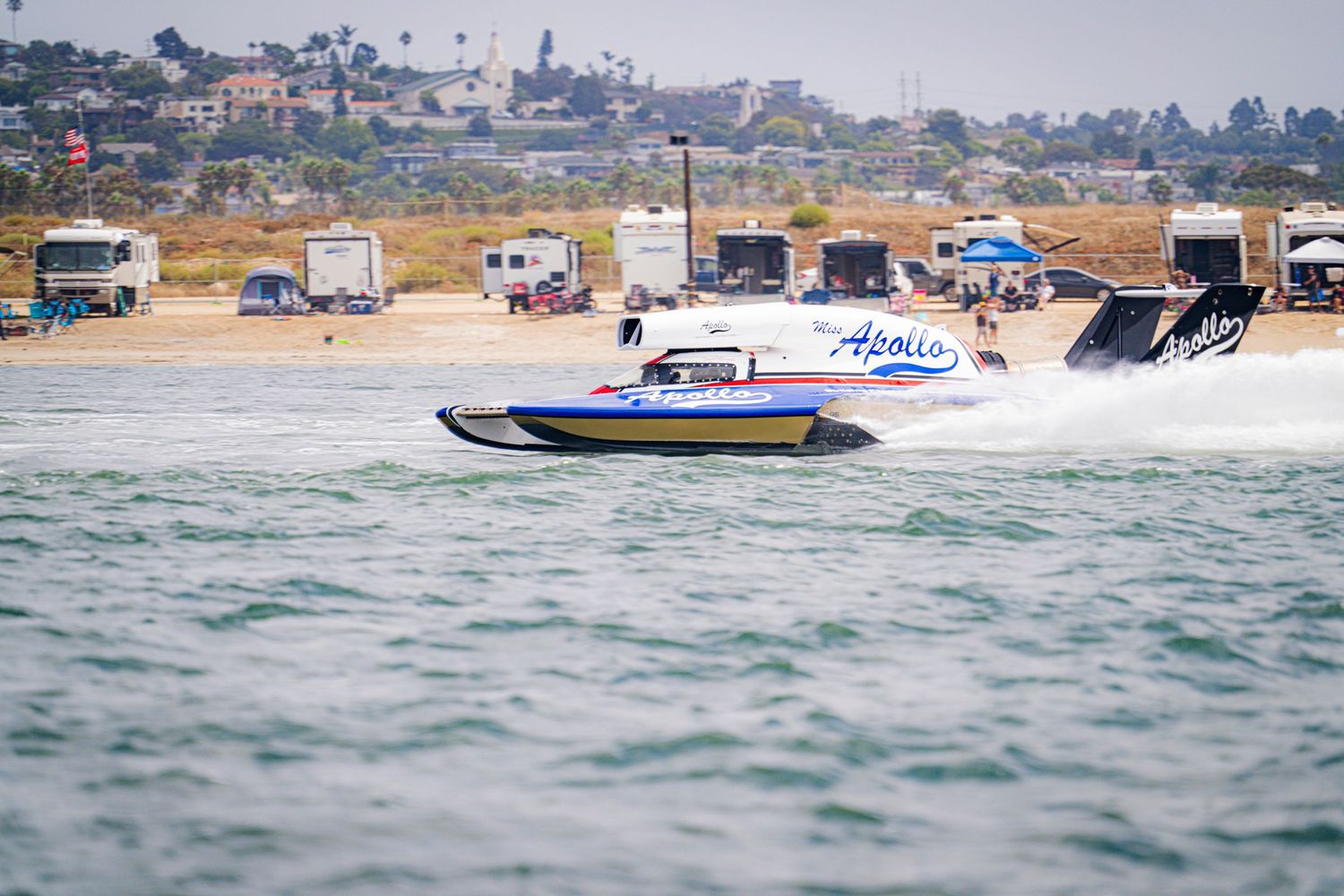 Apollo-branded racing powerboat races at high speed along a coastal waterway during competition.